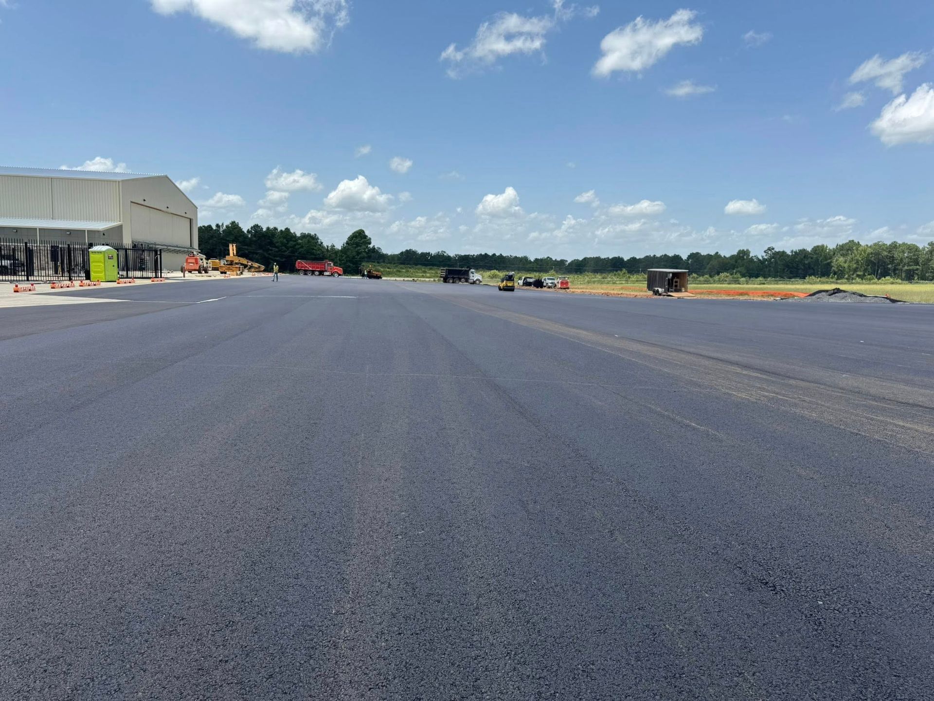 Newly paved asphalt runway stretches toward a hangar under a blue sky.