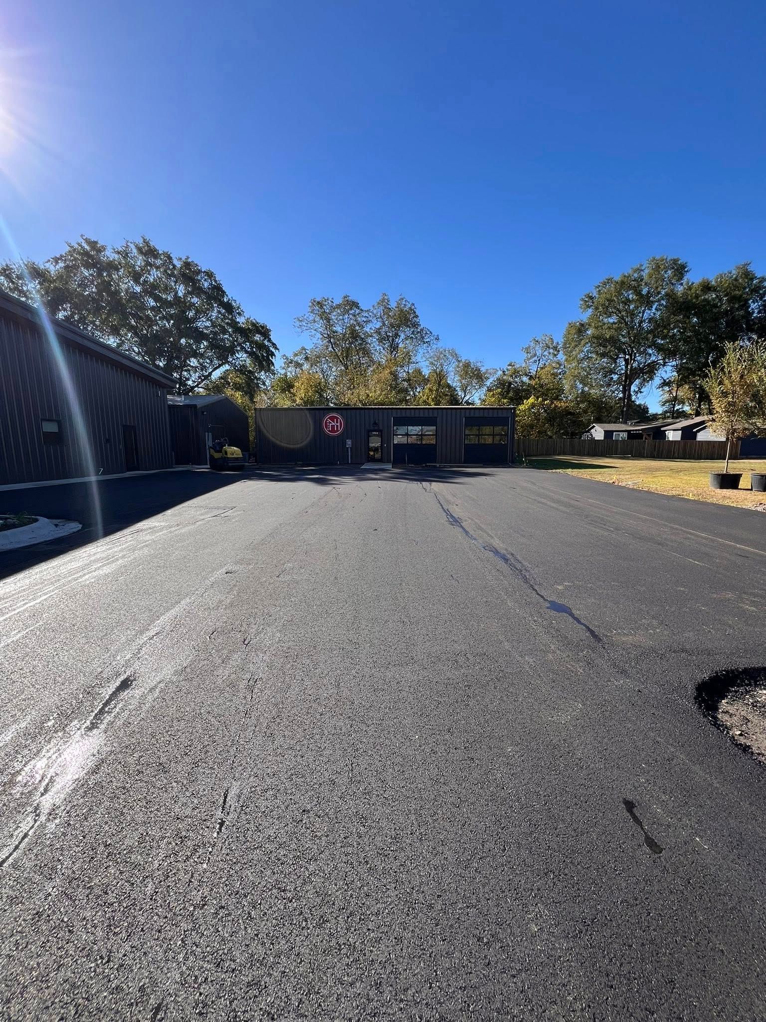 Newly paved asphalt road leads to a dark building under a clear blue sky.