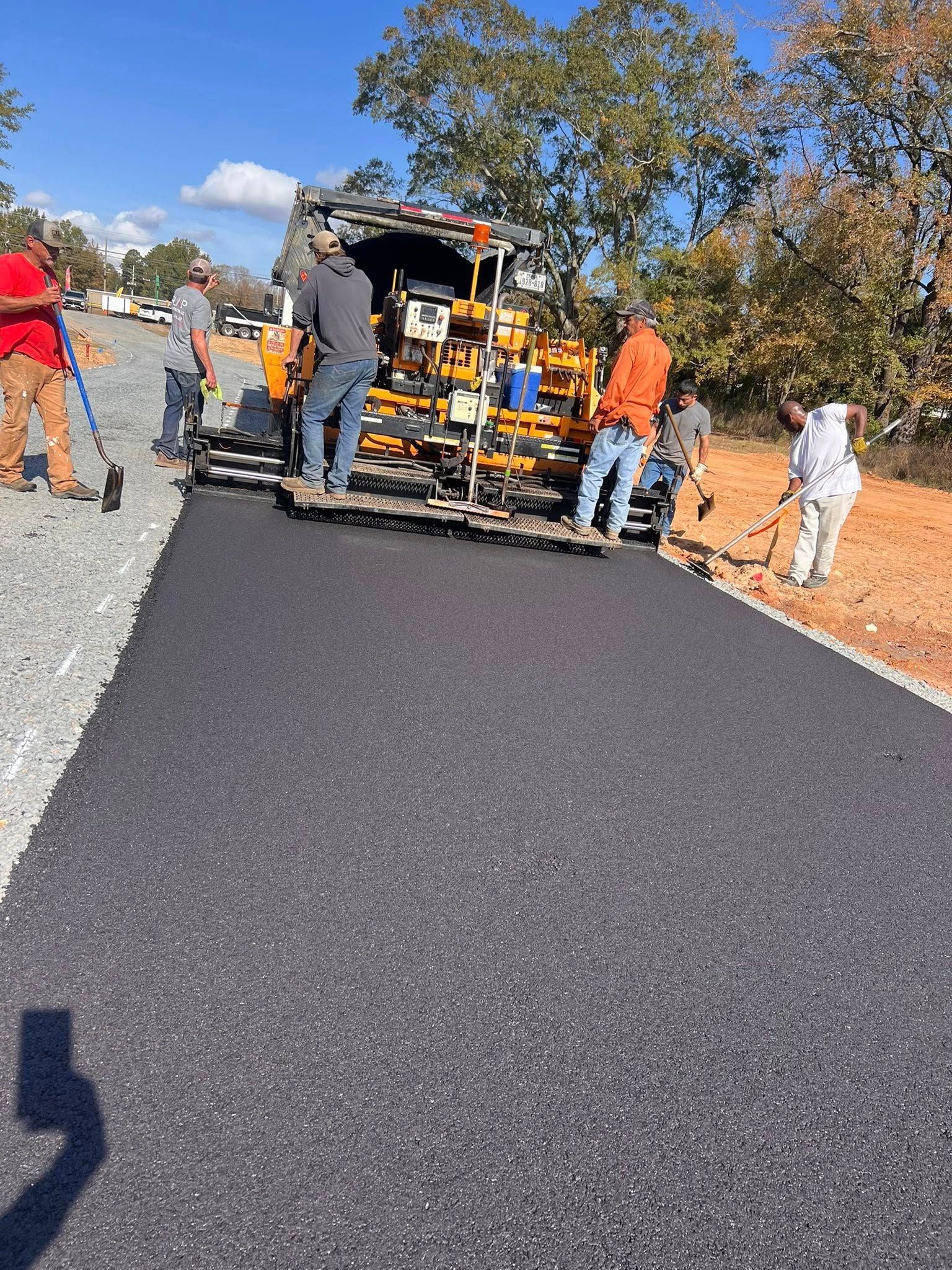 Workers paving a road with asphalt; machinery and several people at work; sunny day.