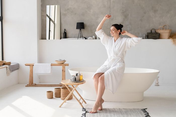 a woman in a bathrobe sits on a bathtub with her arms outstretched