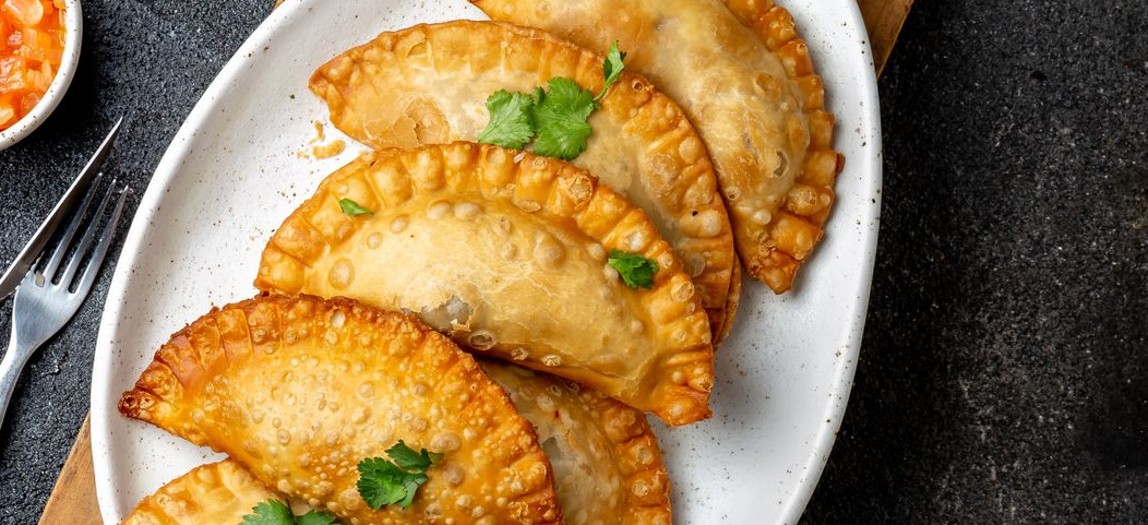 Prato de empanadas douradas decoradas com coentro sobre um fundo escuro.