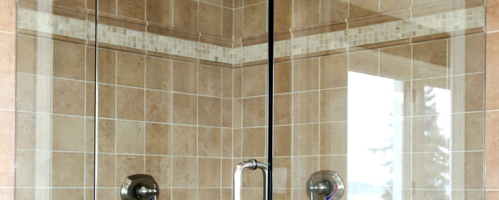 A shower with glass doors and tan tile walls. Chrome hardware is visible.