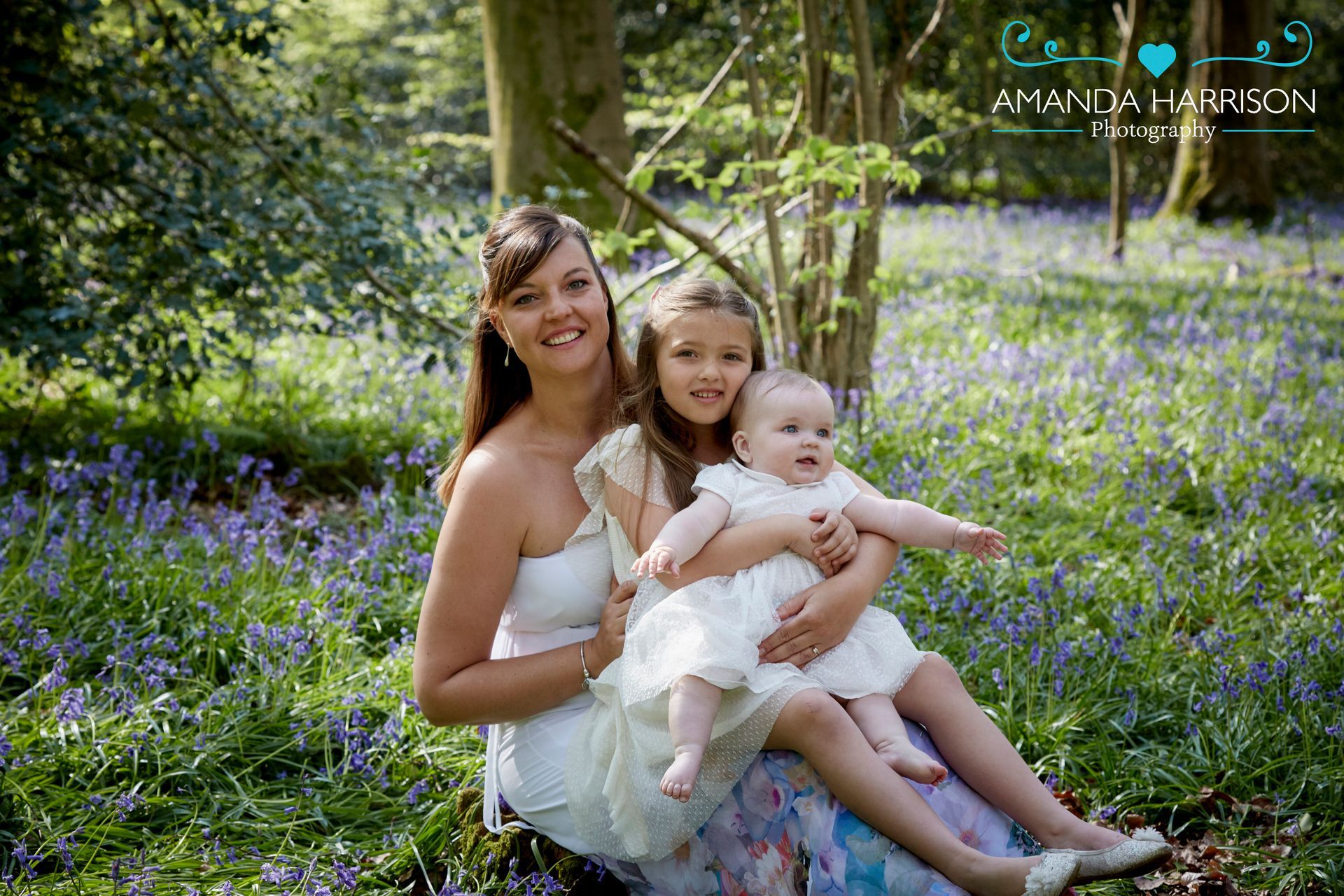 Woman with two children sitting in a purple flower field, smiling at the camera.