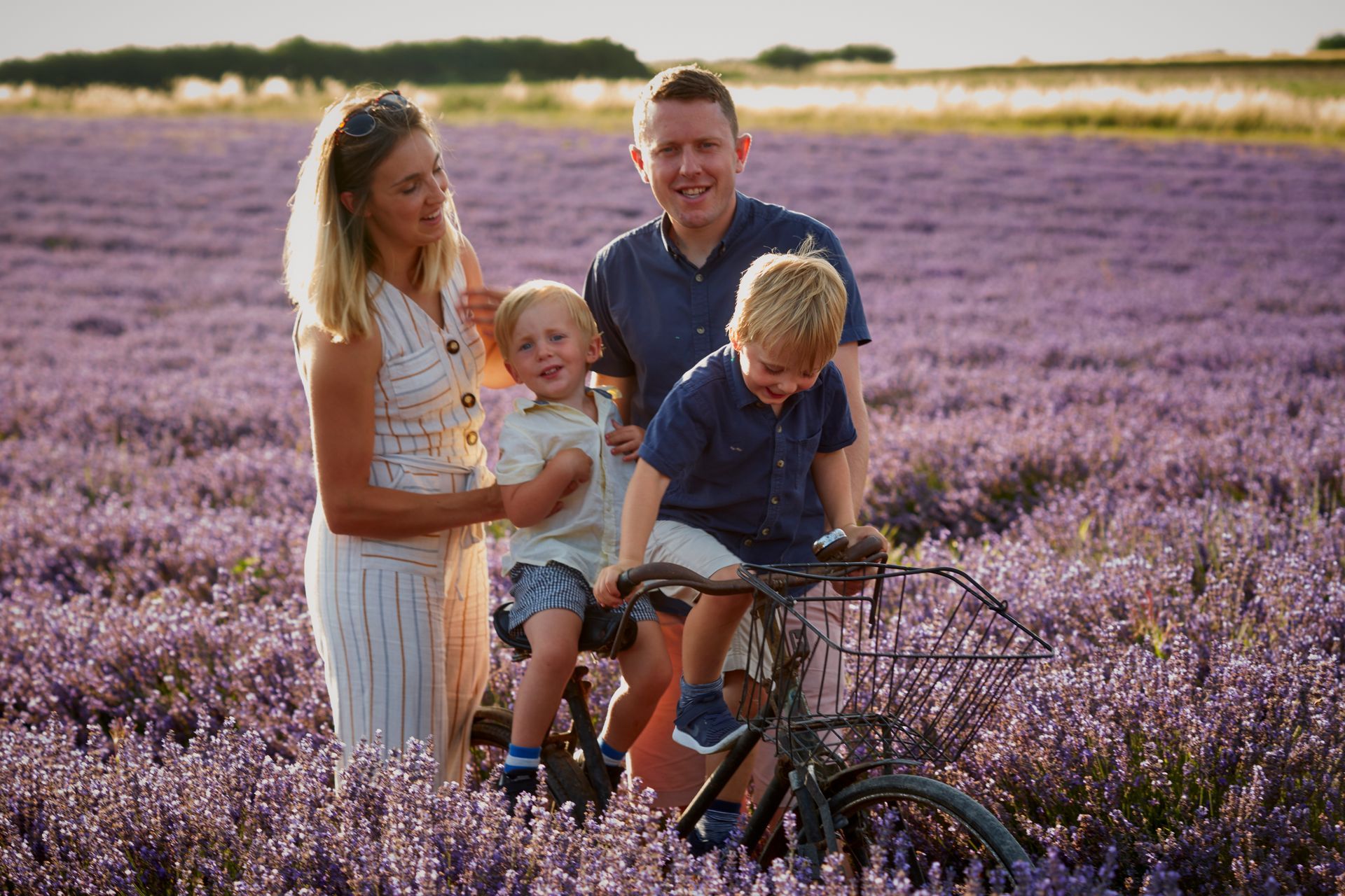 Family standing in a purple flower field, with a child on a bicycle in the foreground.