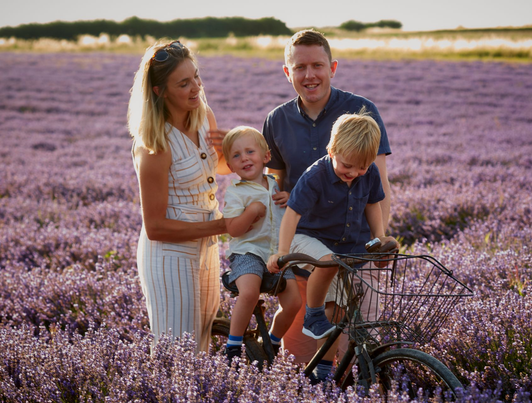 Family with two children in a purple flower field, one child riding a bike and smiling adults standing nearby