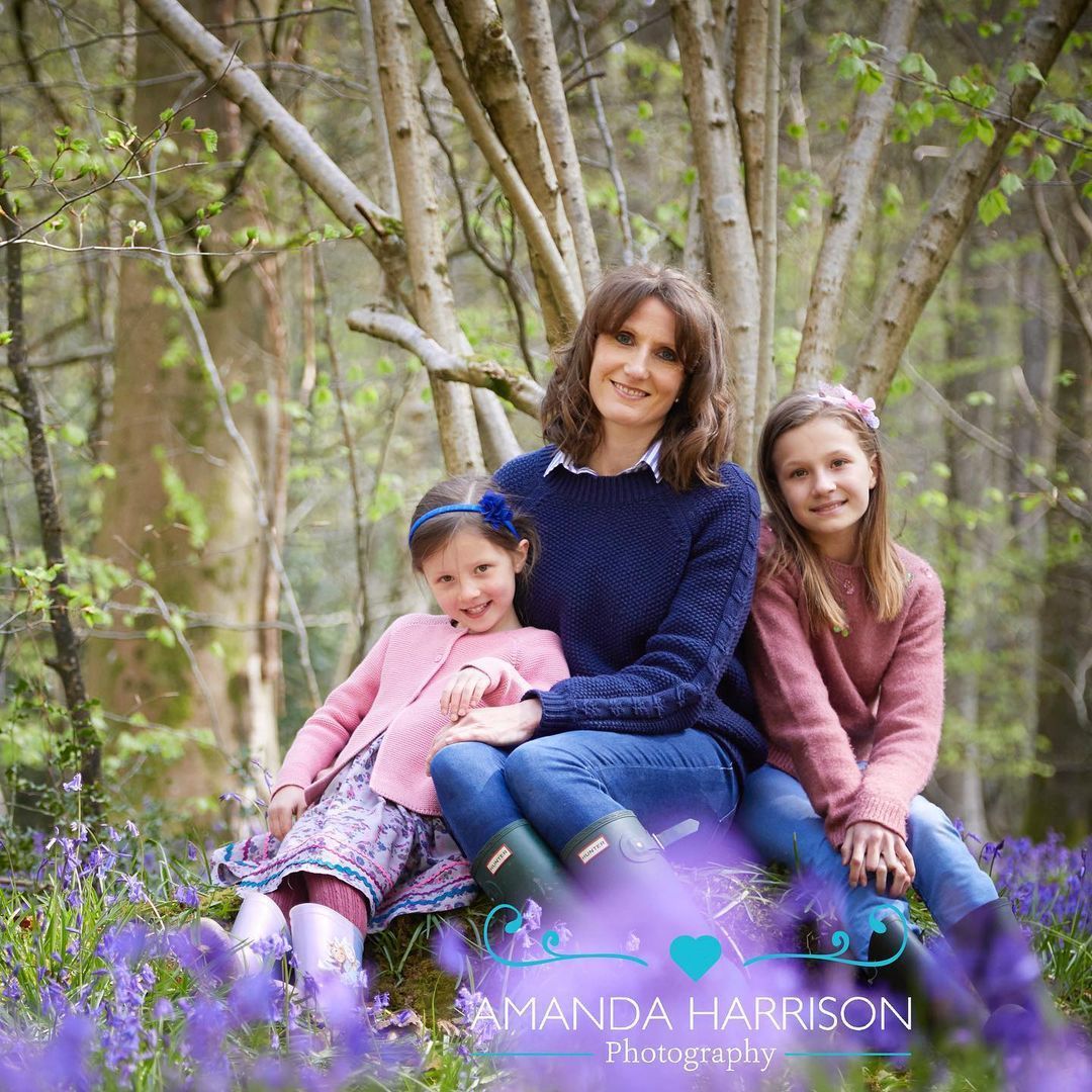 Woman and two children sitting on a log in a wooded area with purple flowers in the foreground