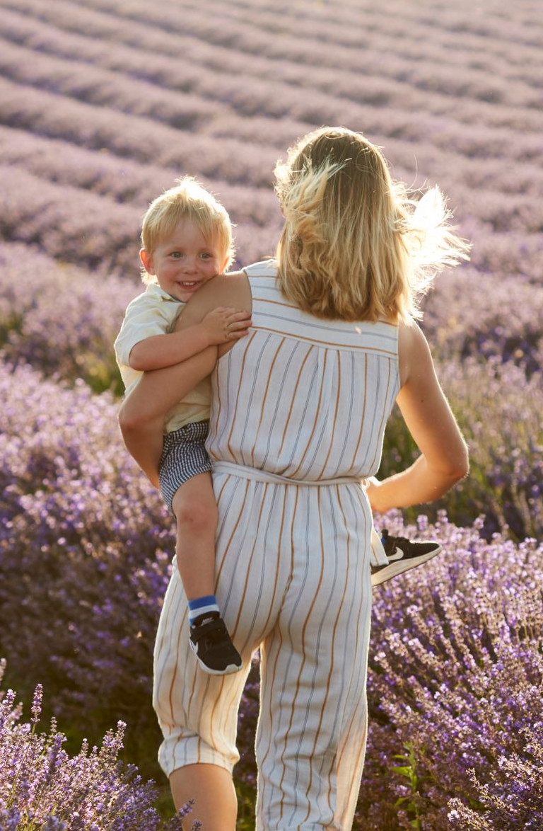 Person carrying a smiling child through a lavender field at sunset