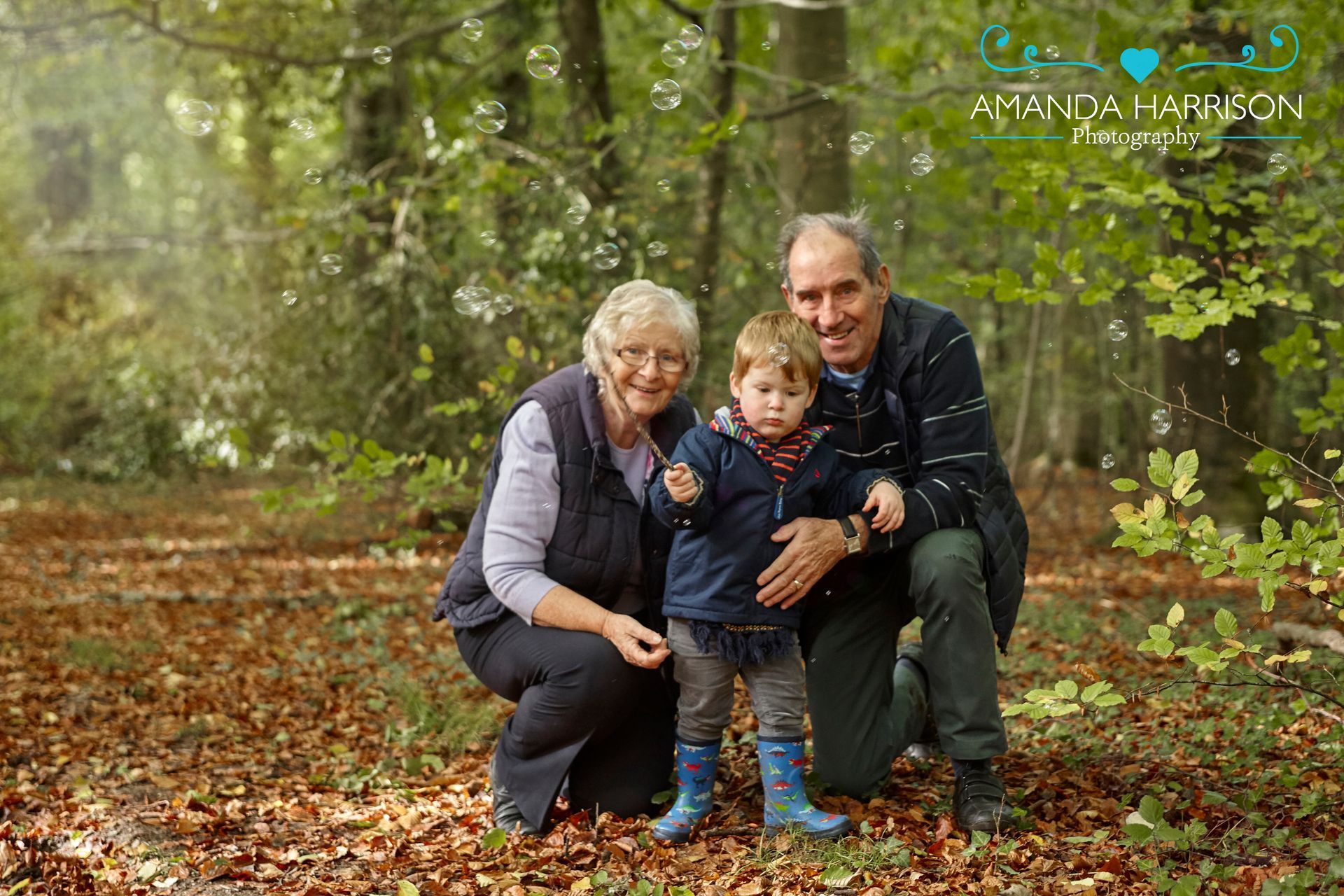 Three people crouch together on a leaf-covered forest path in autumn.