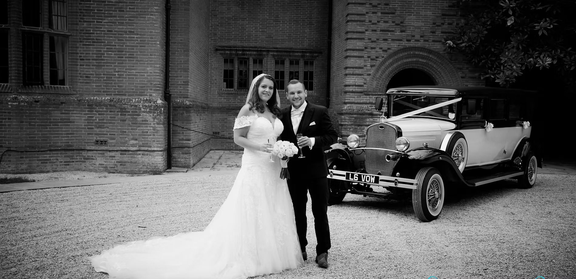 Bride and groom posing beside a vintage car in front of a brick building