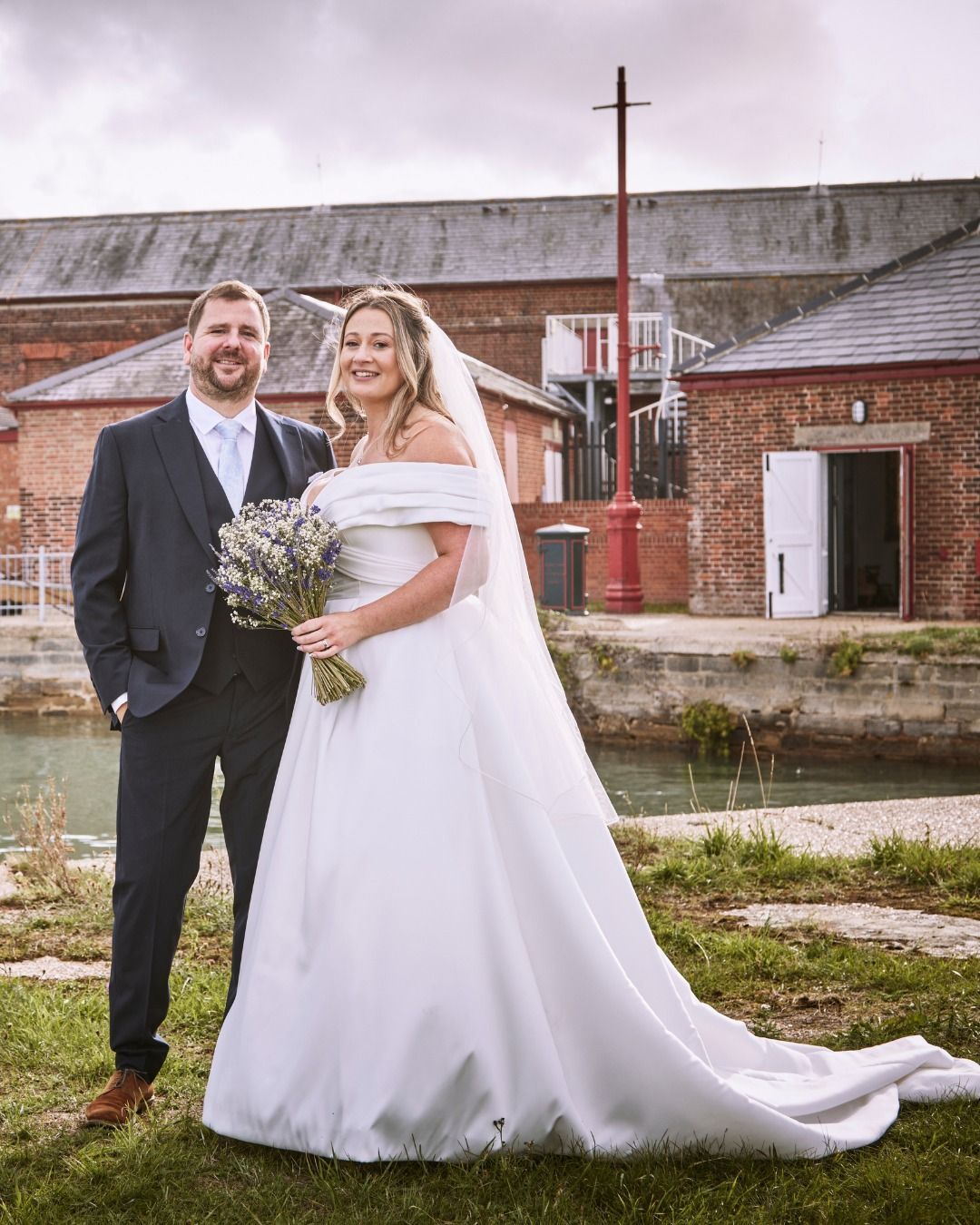 Bride and groom posing outdoors in front of rustic brick buildings on their wedding day