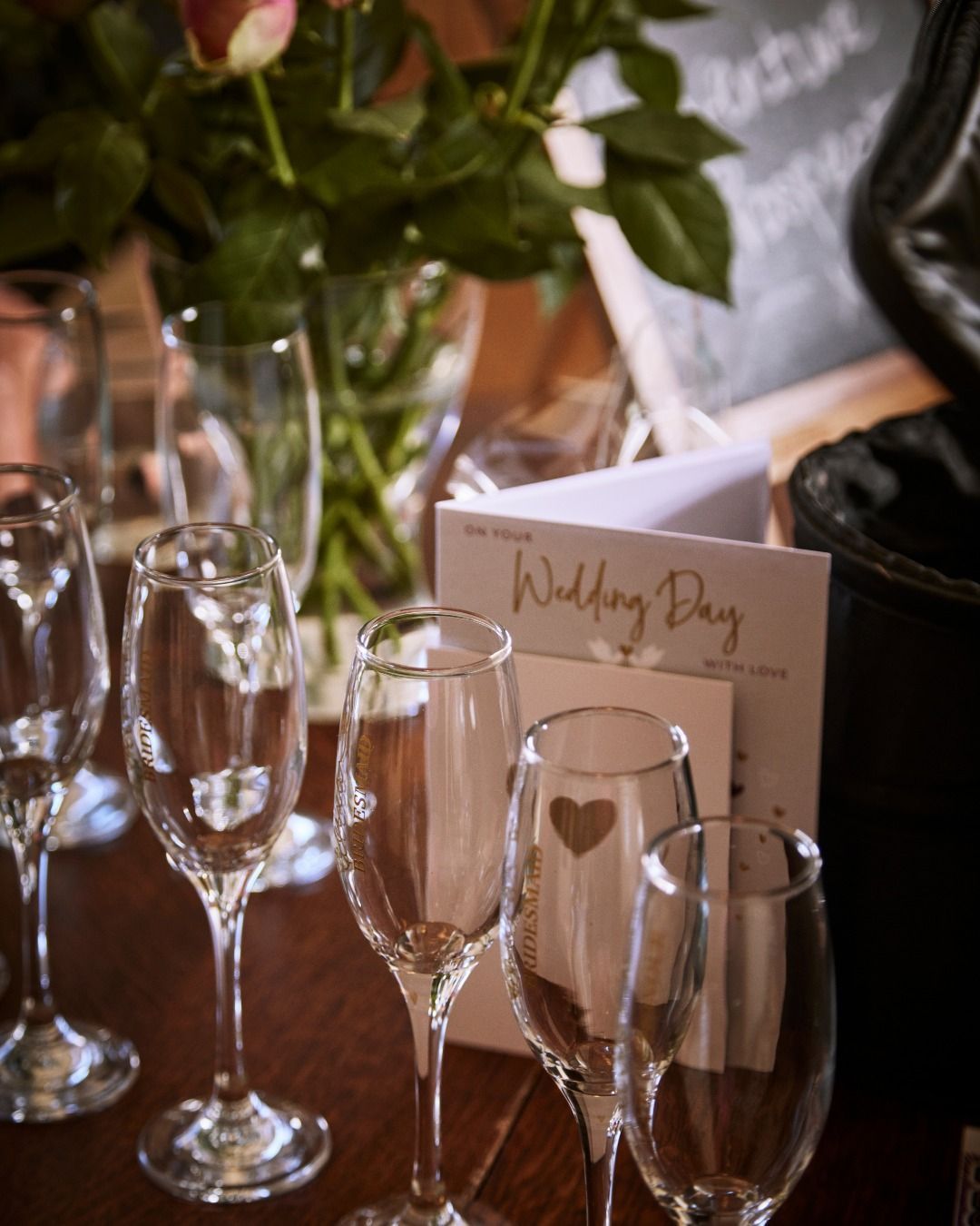 Wine glasses on a table beside a wedding day place card and flowers