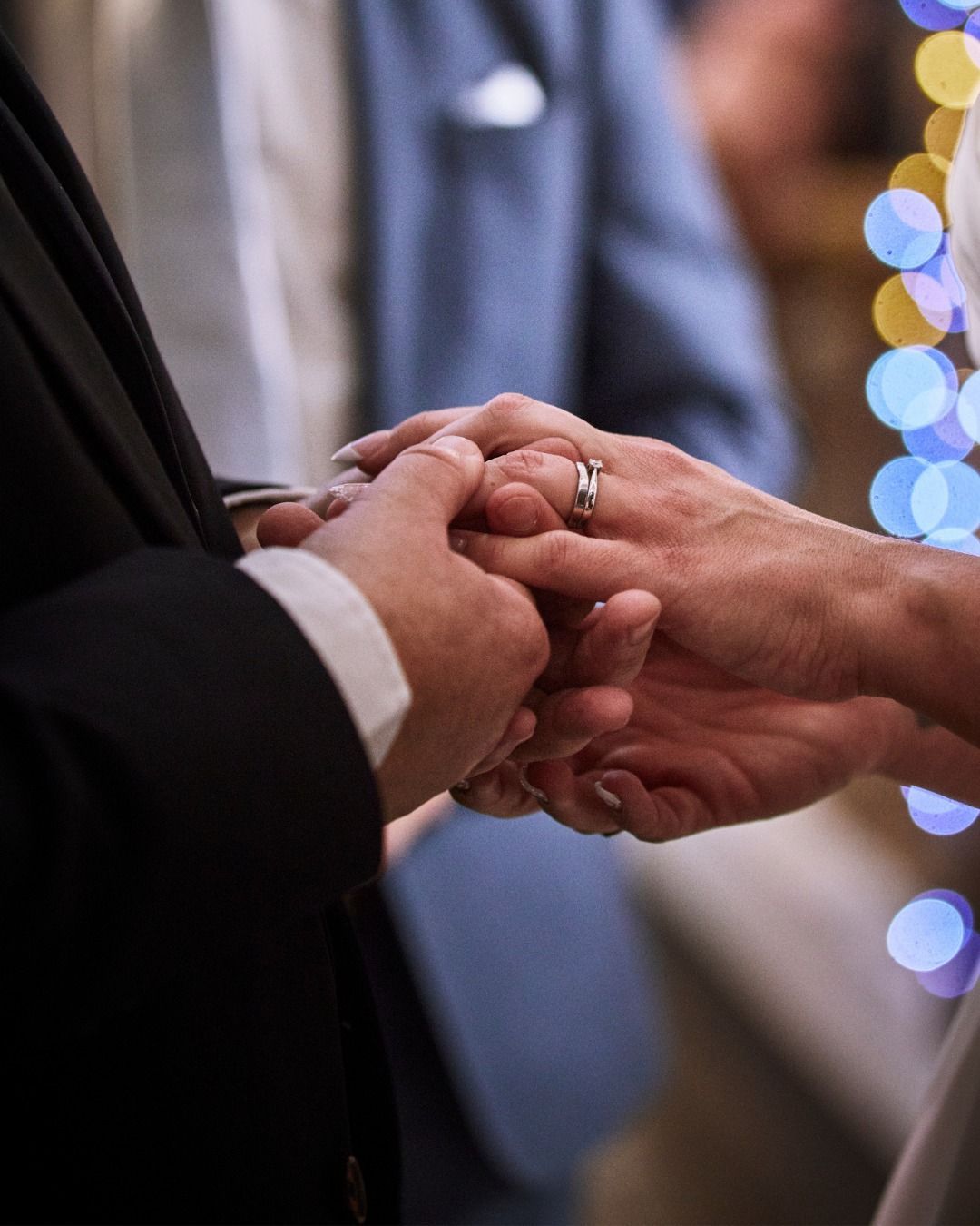 Hands exchanging rings during a wedding ceremony, with soft blue lights in the background