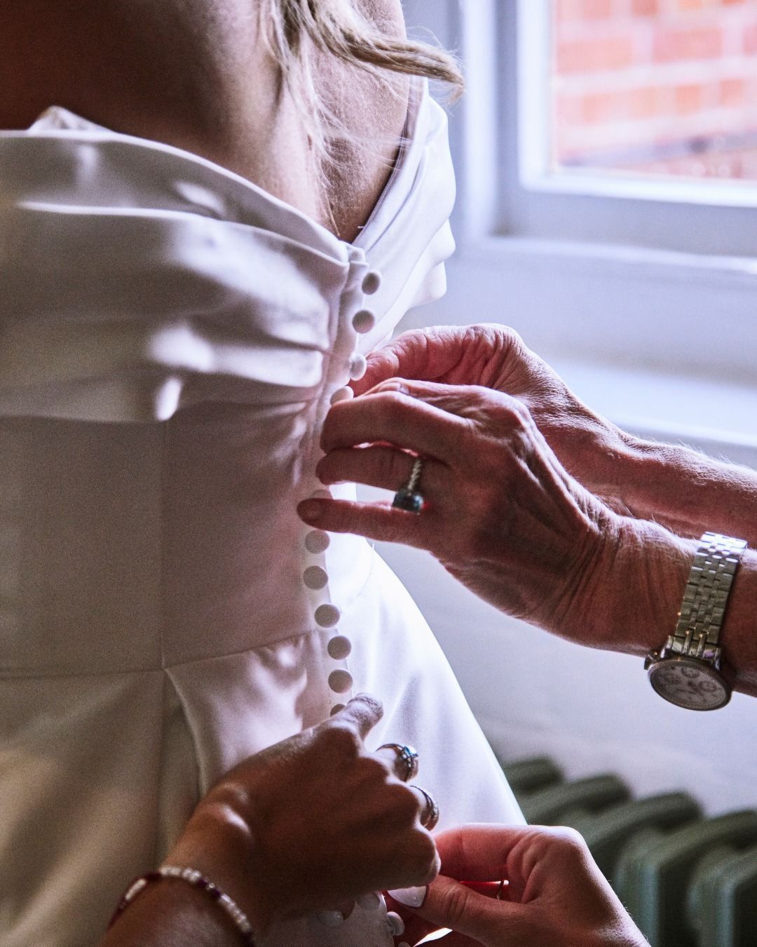 Hands fasten buttons on a white dress by a window