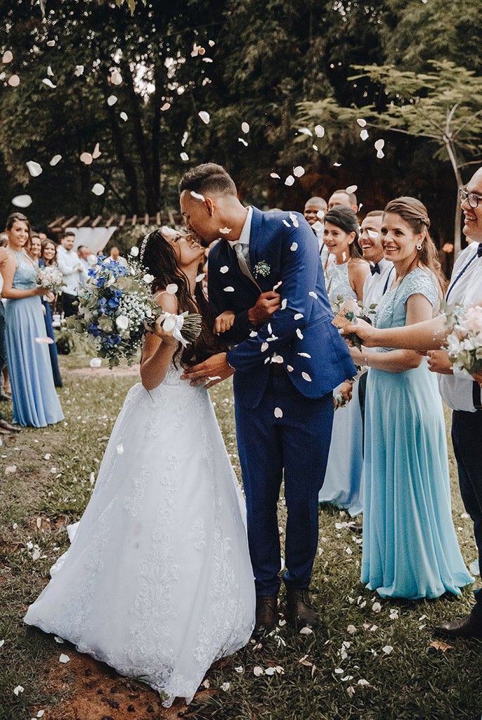 Bride and groom kissing at an outdoor wedding, with bridesmaids in blue dresses around them