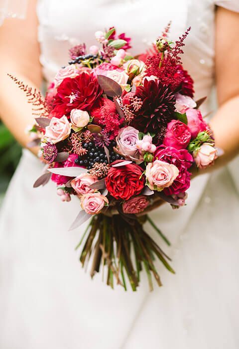 Bridal bouquet of red, pink, and white flowers held against a white wedding dress