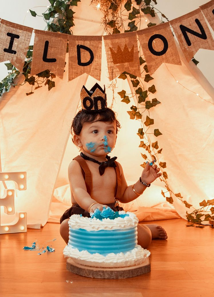 Baby at a first birthday party with a blue-and-white cake and 