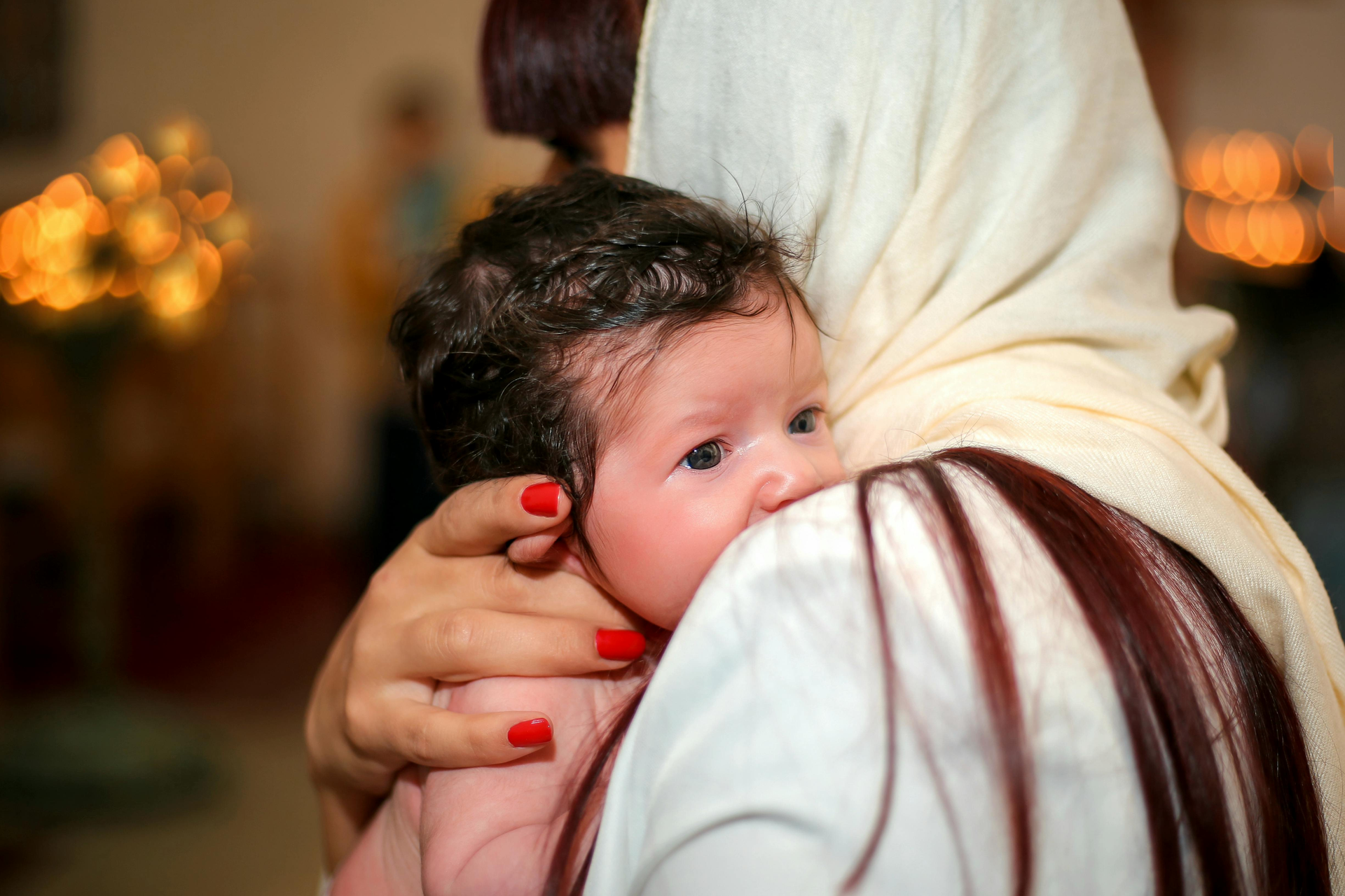 Woman in white headscarf holding a newborn baby close, with soft candlelight in the background