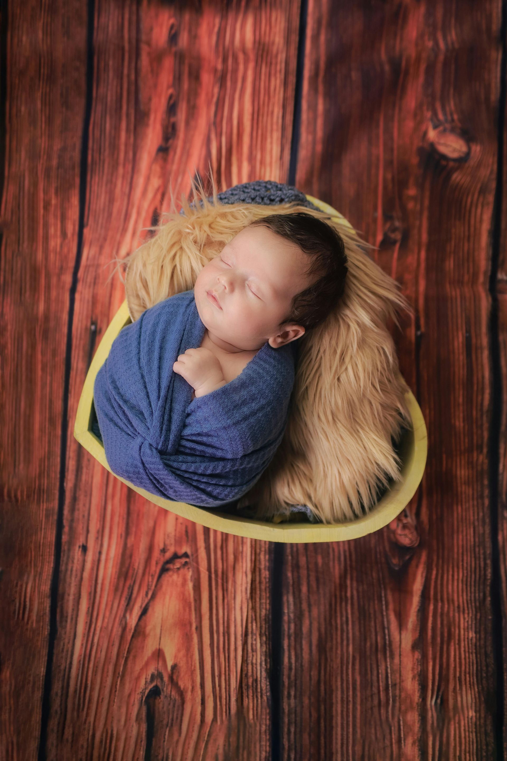 Sleeping baby wrapped in blue on a yellow cushion over a wooden floor