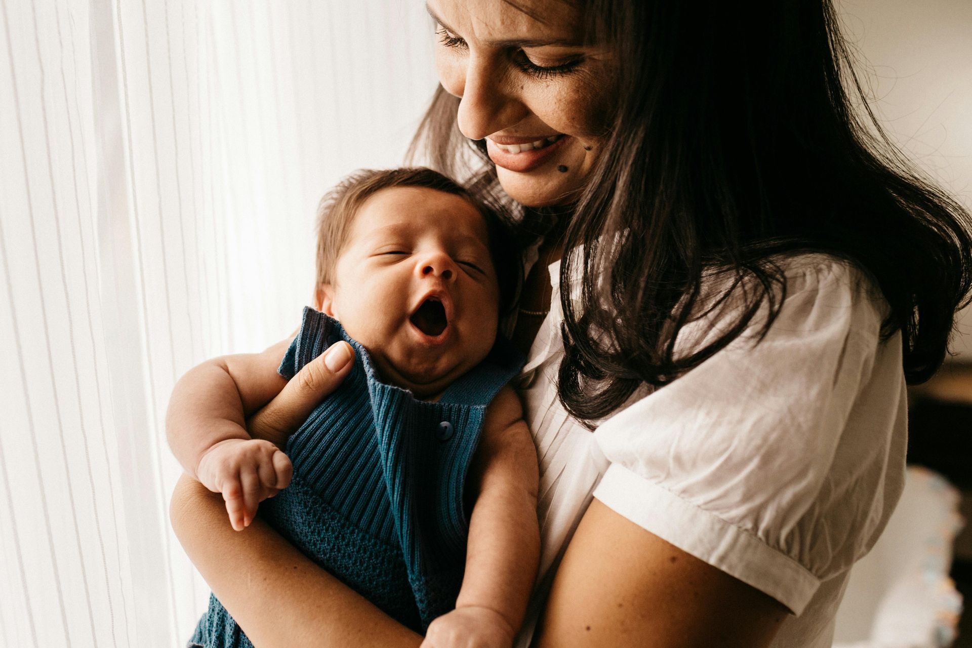 Mother holding yawning baby in a softly lit room