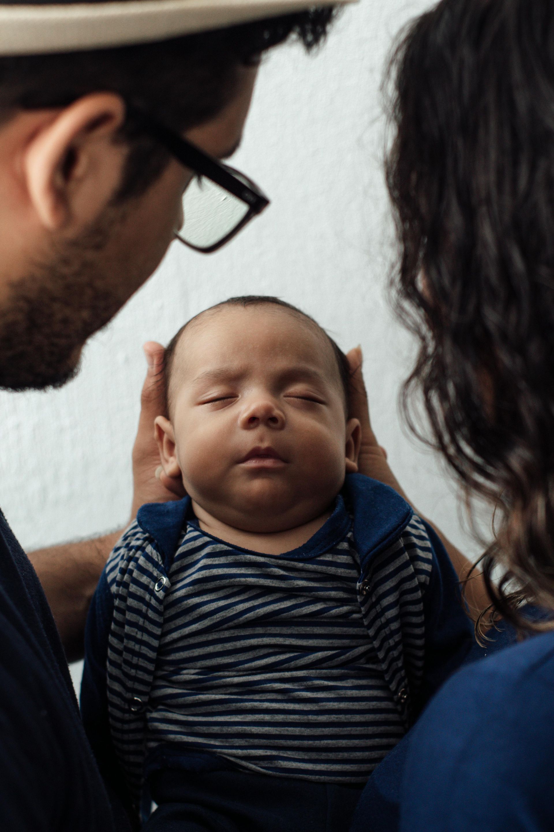 Baby asleep between two adults holding its head gently