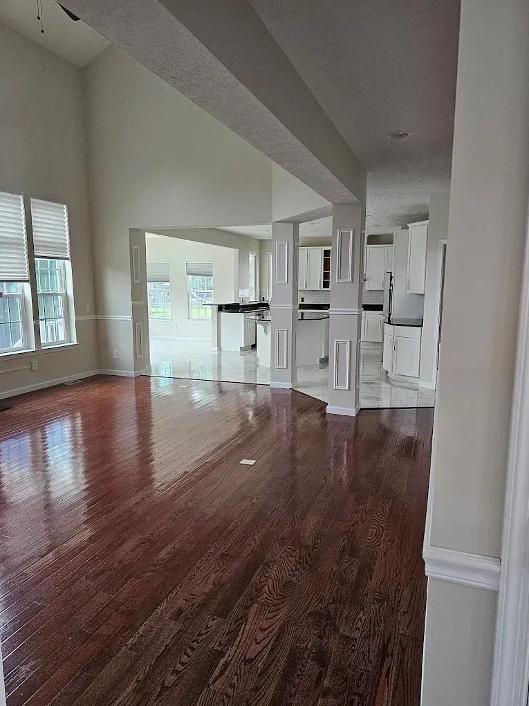 Interior of a home with wood floors, white walls, and a view into the kitchen area.