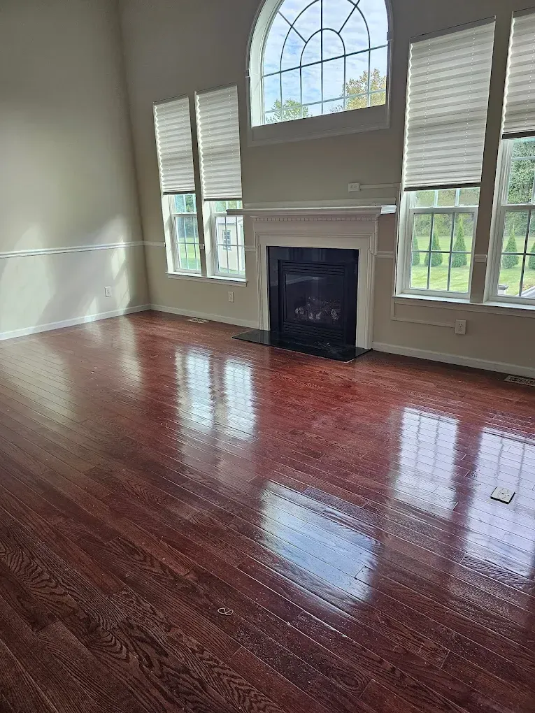 A living room with polished reddish-brown hardwood floors, fireplace, and arched window with blinds.