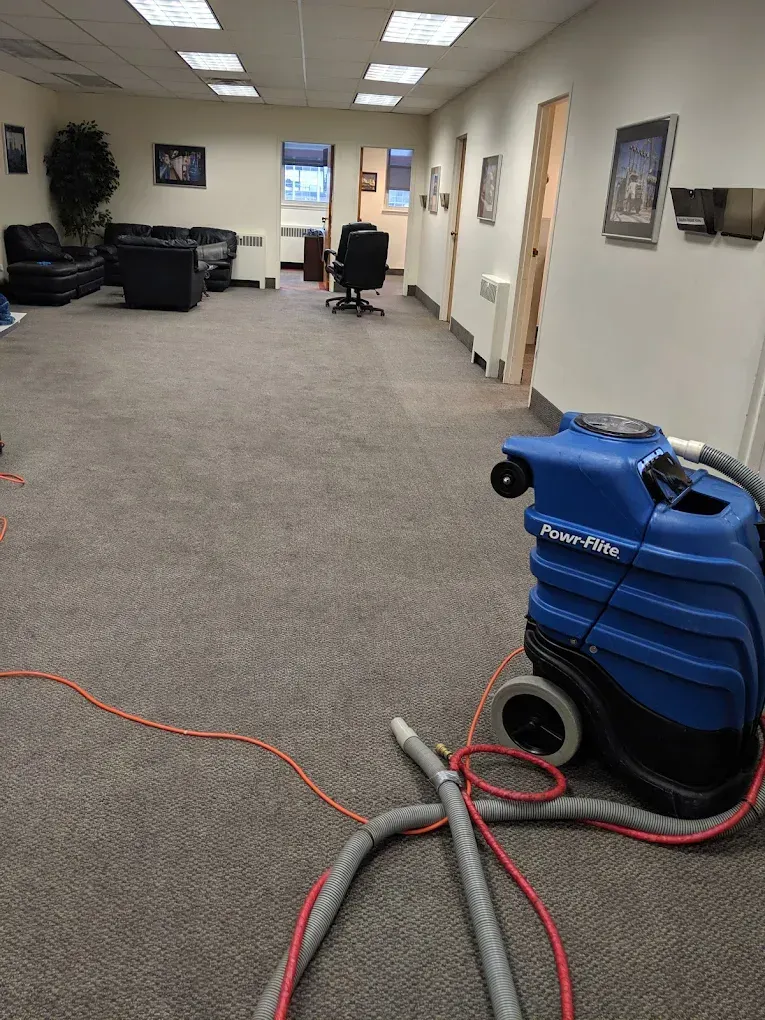 Office cleaning crew using sprayers, wearing blue aprons and gloves, in an office.