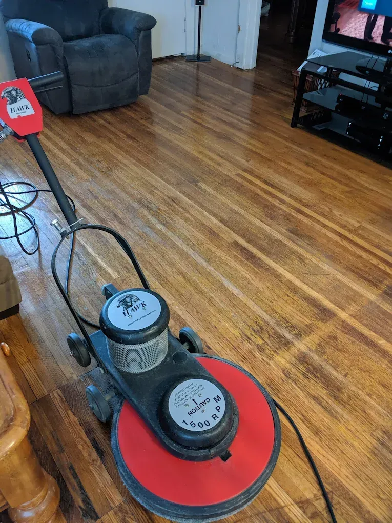 Person kneeling, scrubbing a tile floor with a brush; cleaning supplies visible; hallway setting.