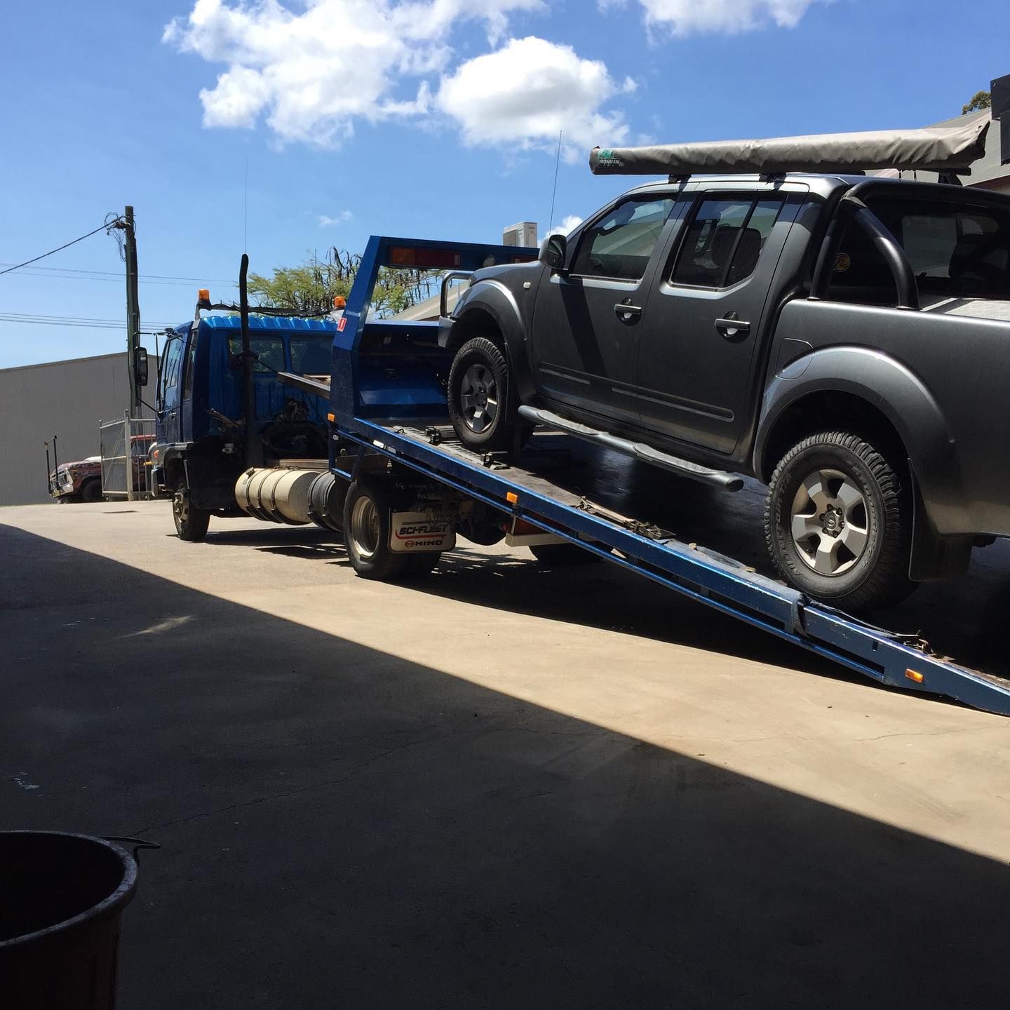 A gray pickup truck being loaded onto a blue tow truck on a sunny day — Bangalow Towing in Bangalow, NSW