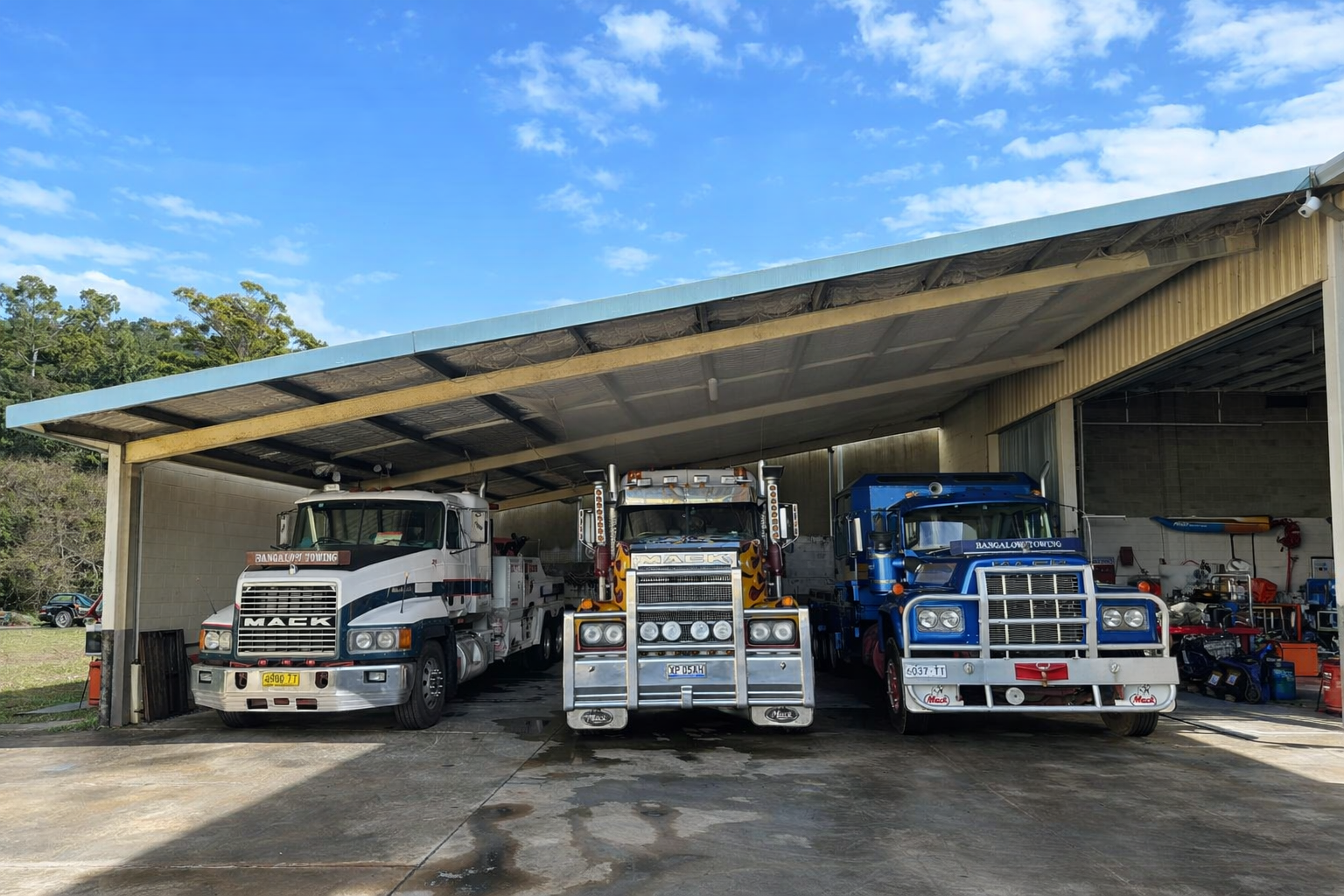 Three semi-trucks parked under a corrugated metal shelter — Bangalow Towing in Bangalow, NSW