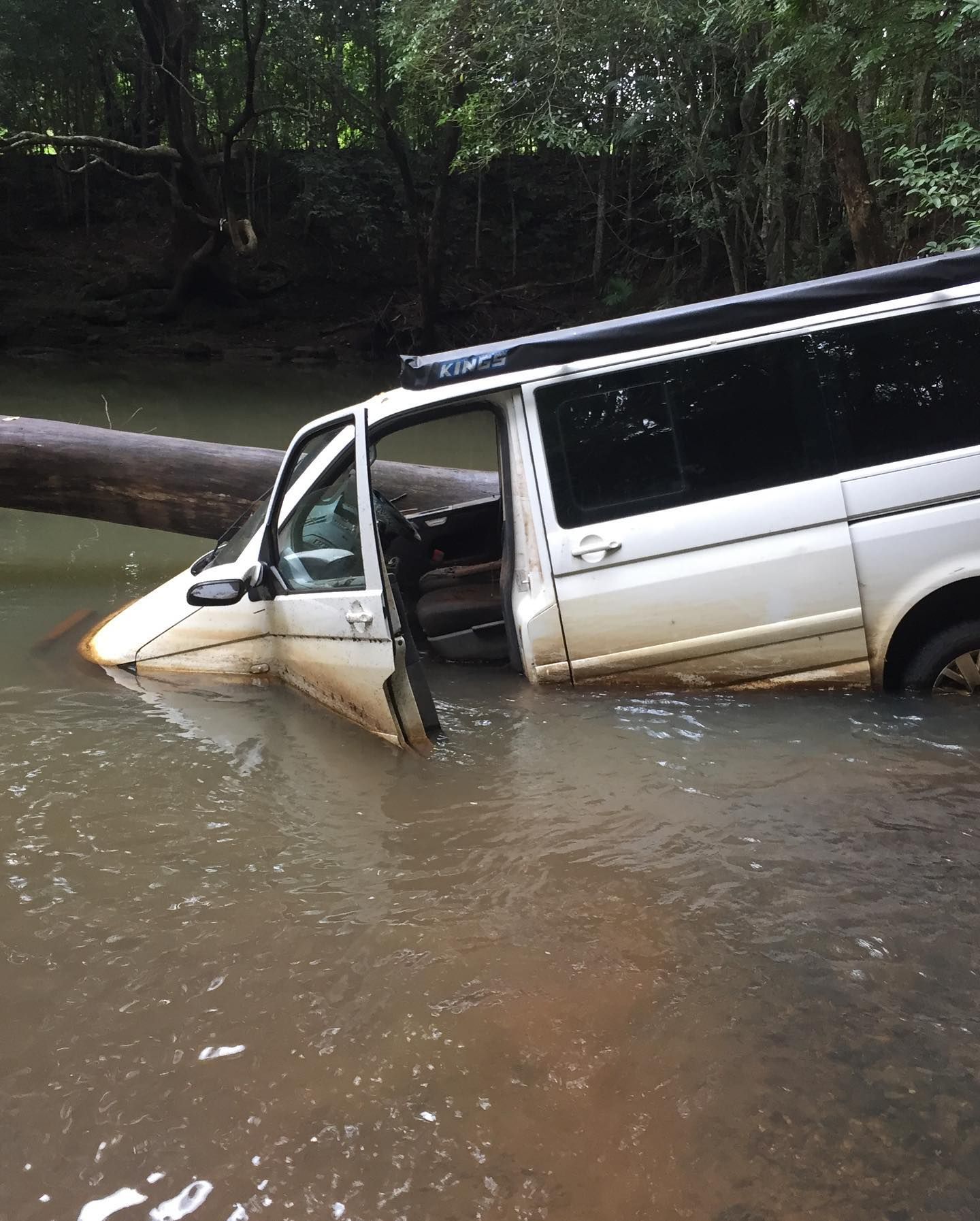 White van submerged in a murky river, door open, leaning against a log — Bangalow Towing in Bangalow, NSW