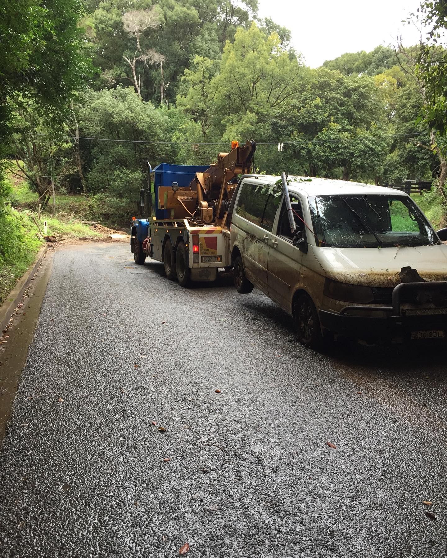 Tow truck pulling a white van on a wet, gravel road surrounded by trees — Bangalow Towing in Bangalow, NSW