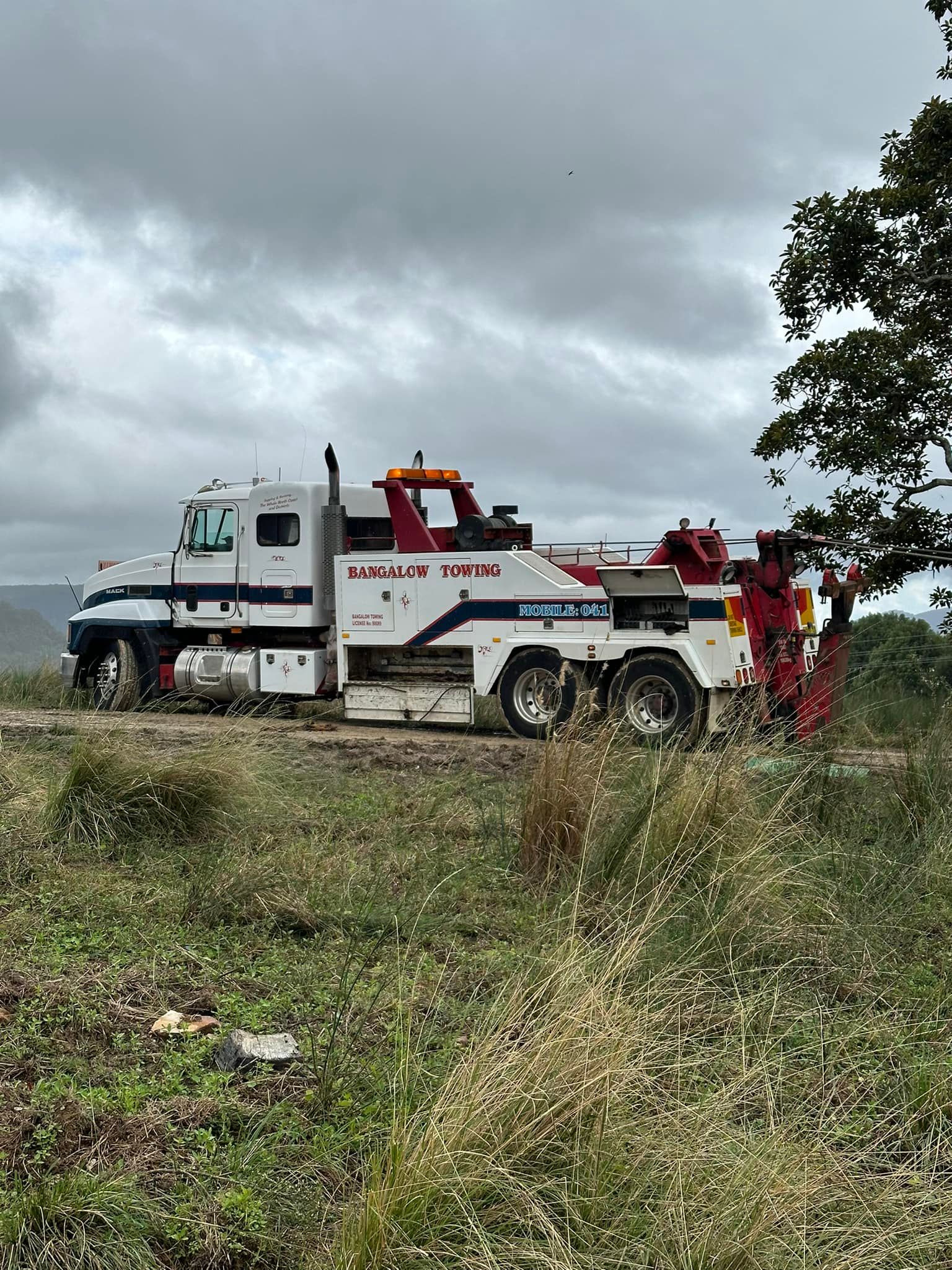 White tow truck on a dirt road, cloudy sky, red and blue accents, grass in the foreground — Bangalow Towing in Bangalow, NSW