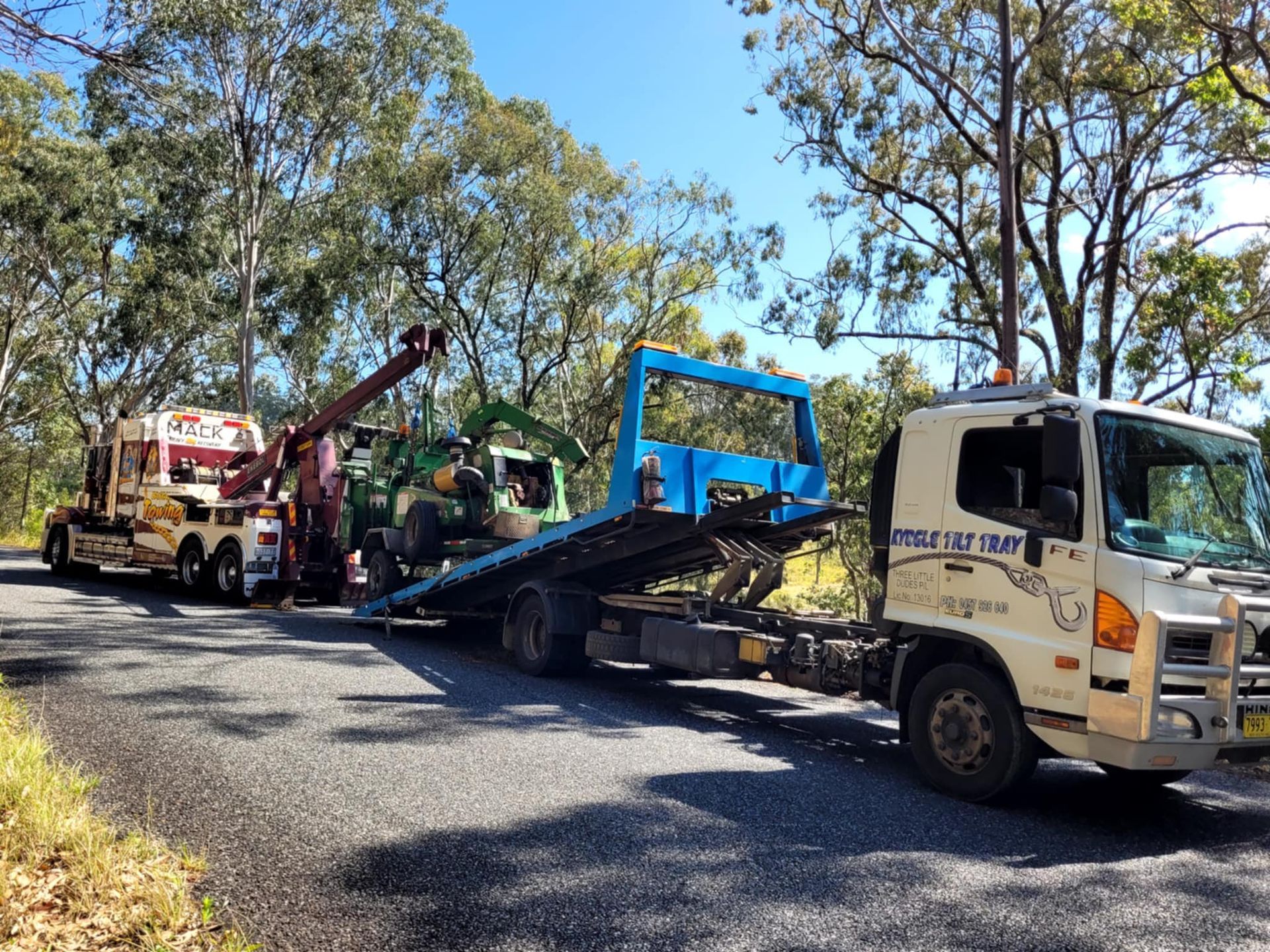 Tow truck loading a blue vehicle on a flatbed beside a road lined with trees — Bangalow Towing in Bangalow, NSW