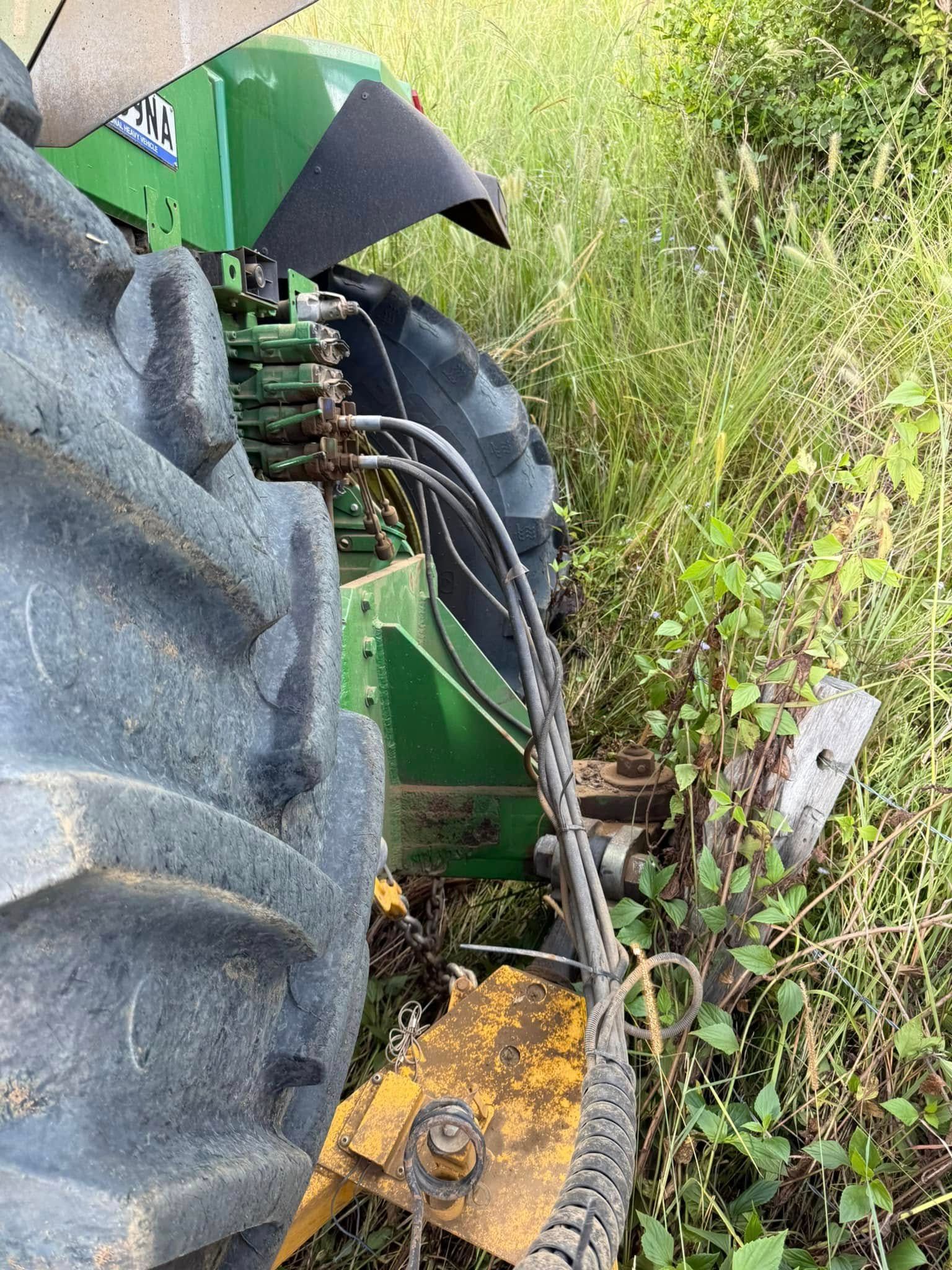 Green Tractor Tire Next to Tall Grass and a Yellow Attachment — Bangalow Towing in Bangalow, NSW
