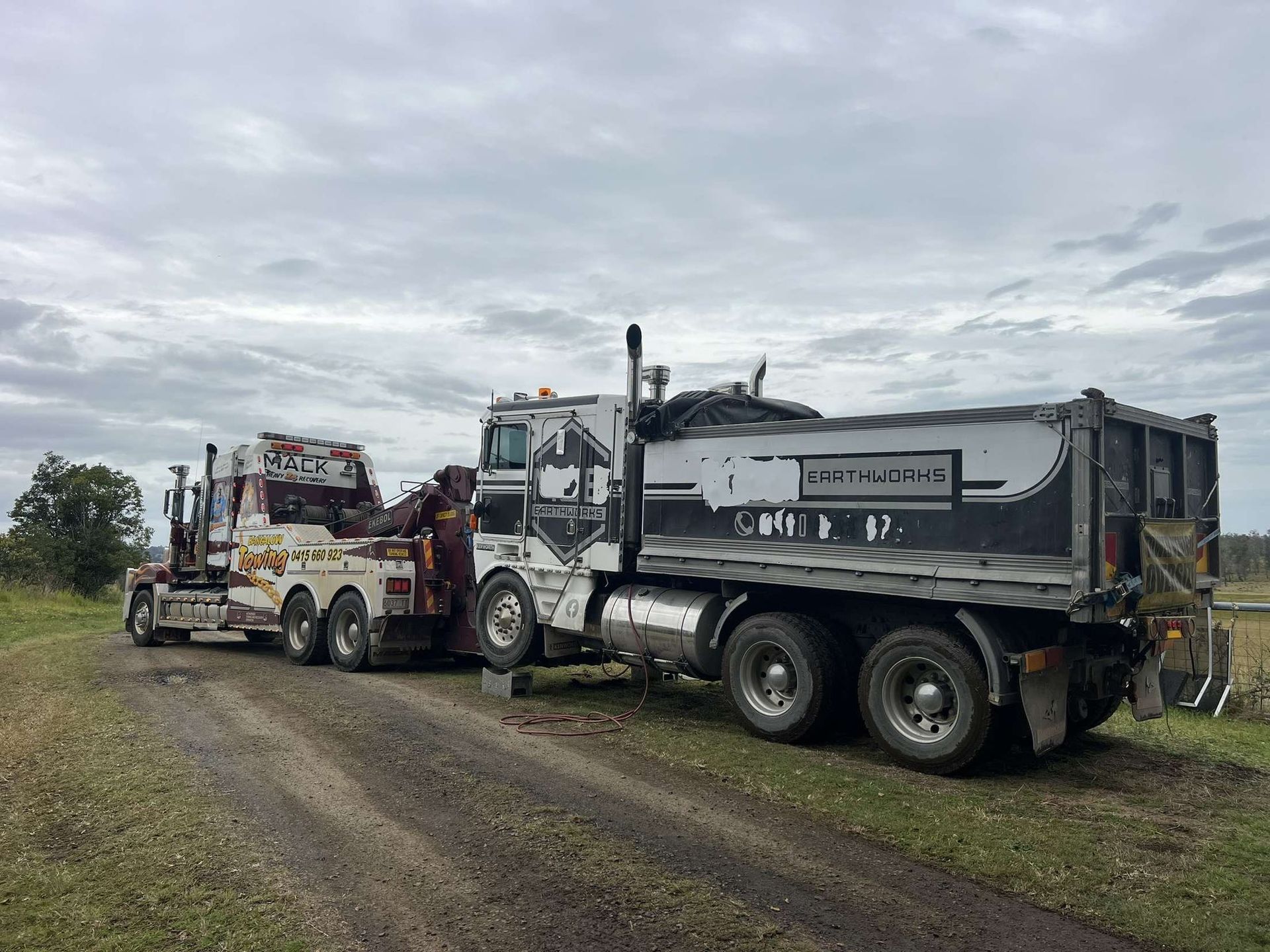 Tow truck pulling a dump truck on a dirt road under a cloudy sky — Bangalow Towing in Bangalow, NSW