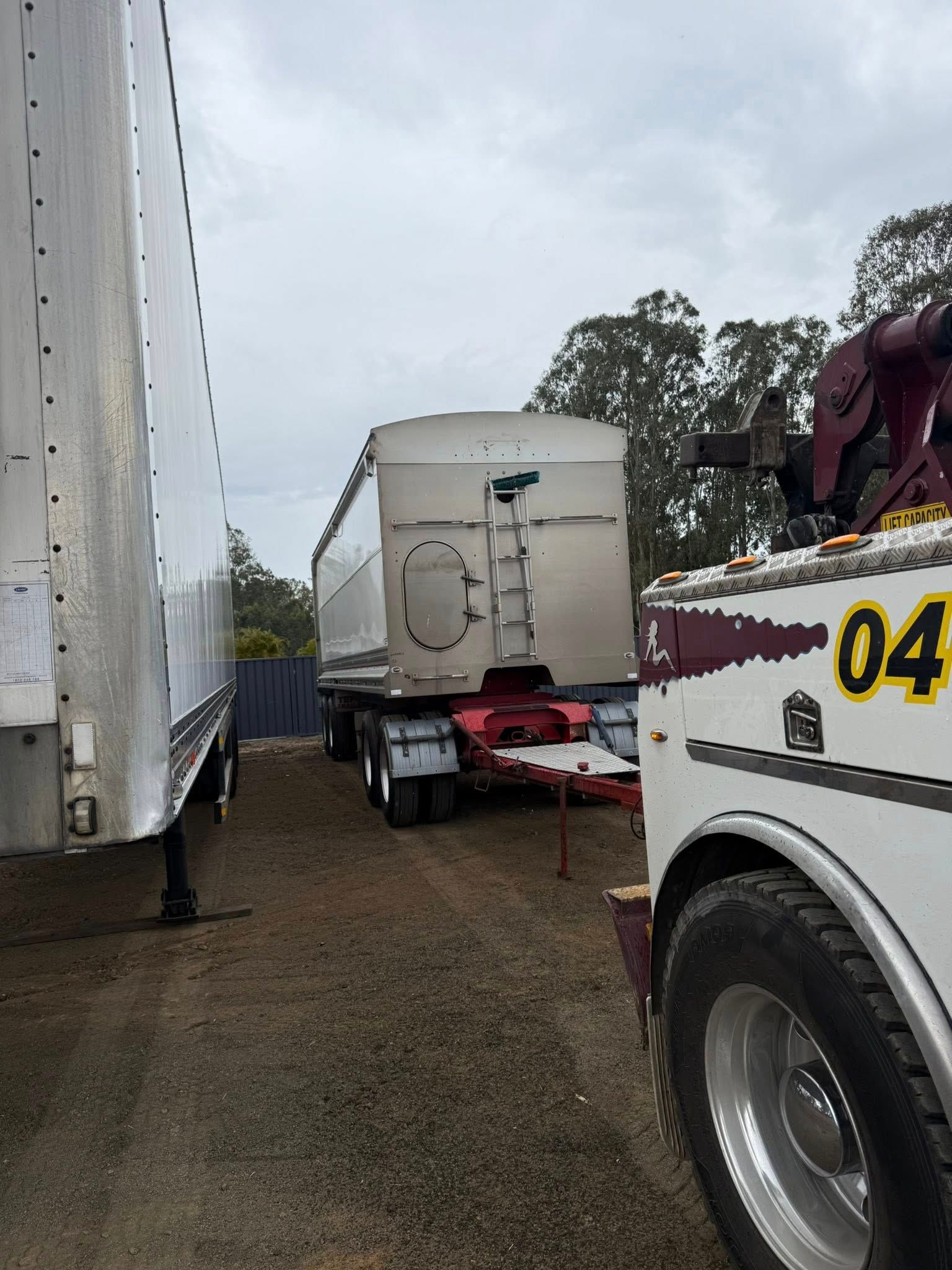 Truck and trailer parked on gravel, with a tow truck nearby under an overcast sky — Bangalow Towing in Bangalow, NSW