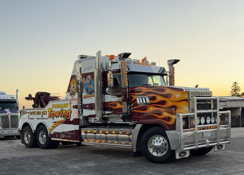 Decorative orange and chrome tow truck parked outdoors at sunset with other trucks nearby — Bangalow Towing in Bangalow, NSW