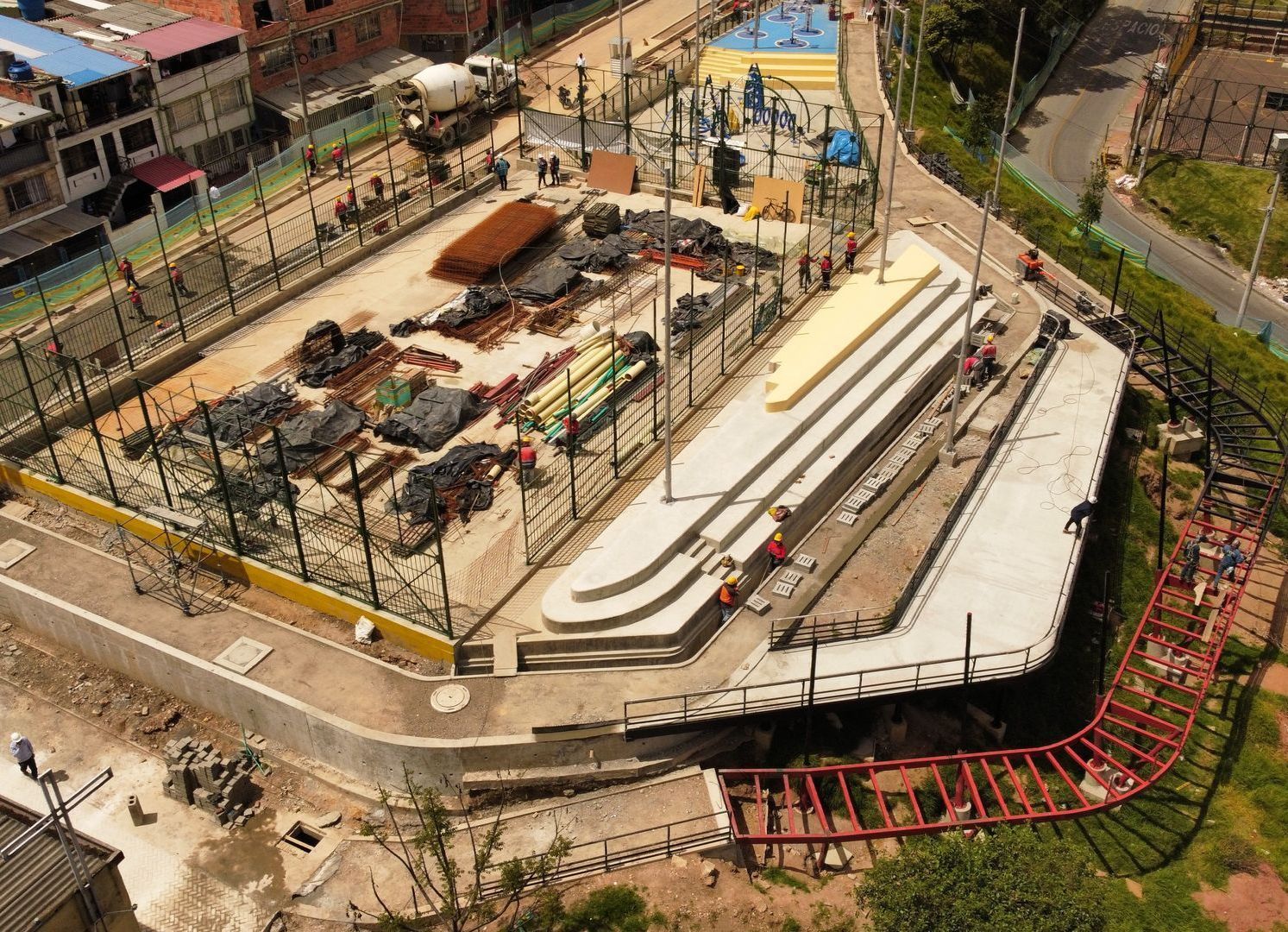Una vista aérea de un parque en construcción con una montaña rusa al fondo.