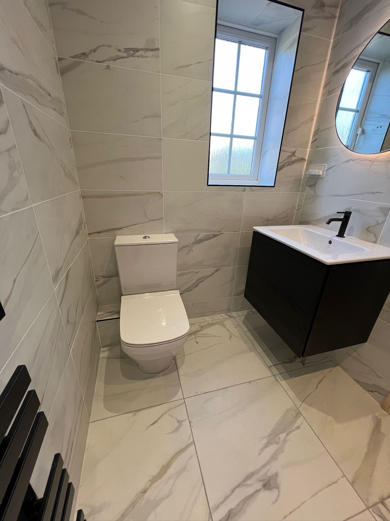 A bathroom with a toilet , sink , mirror and window.