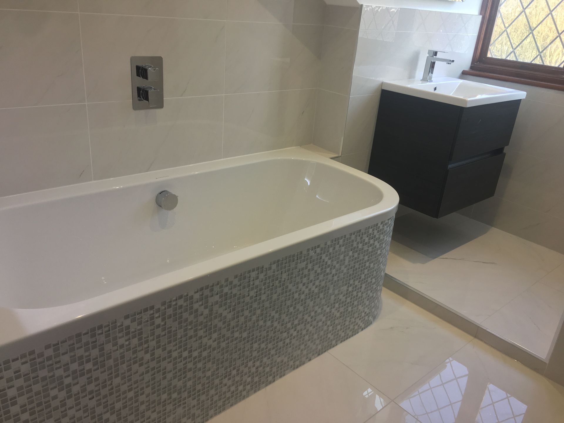 A bathroom with a bathtub , sink , and window.