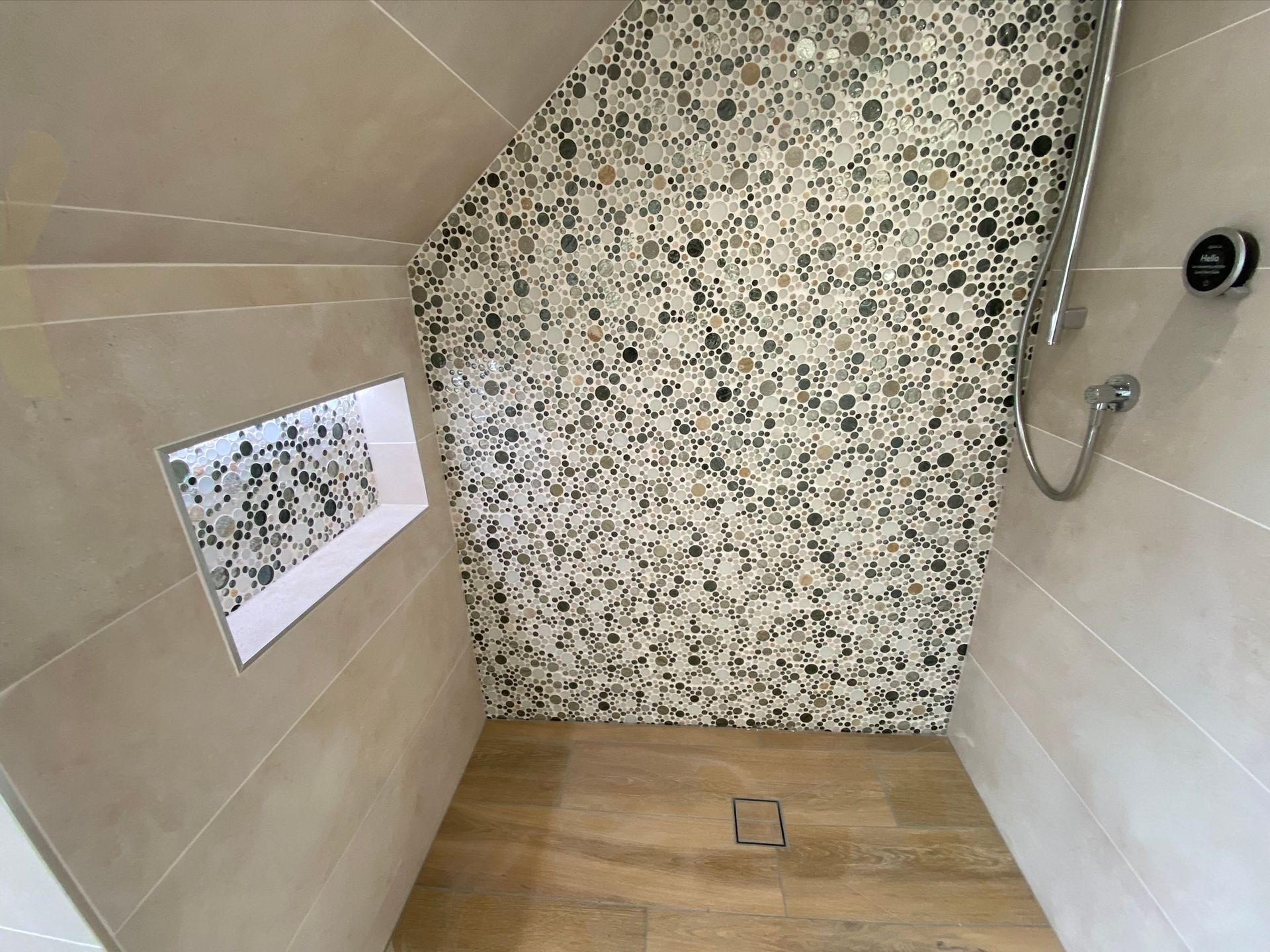 A shower with a tiled wall and a wooden floor.