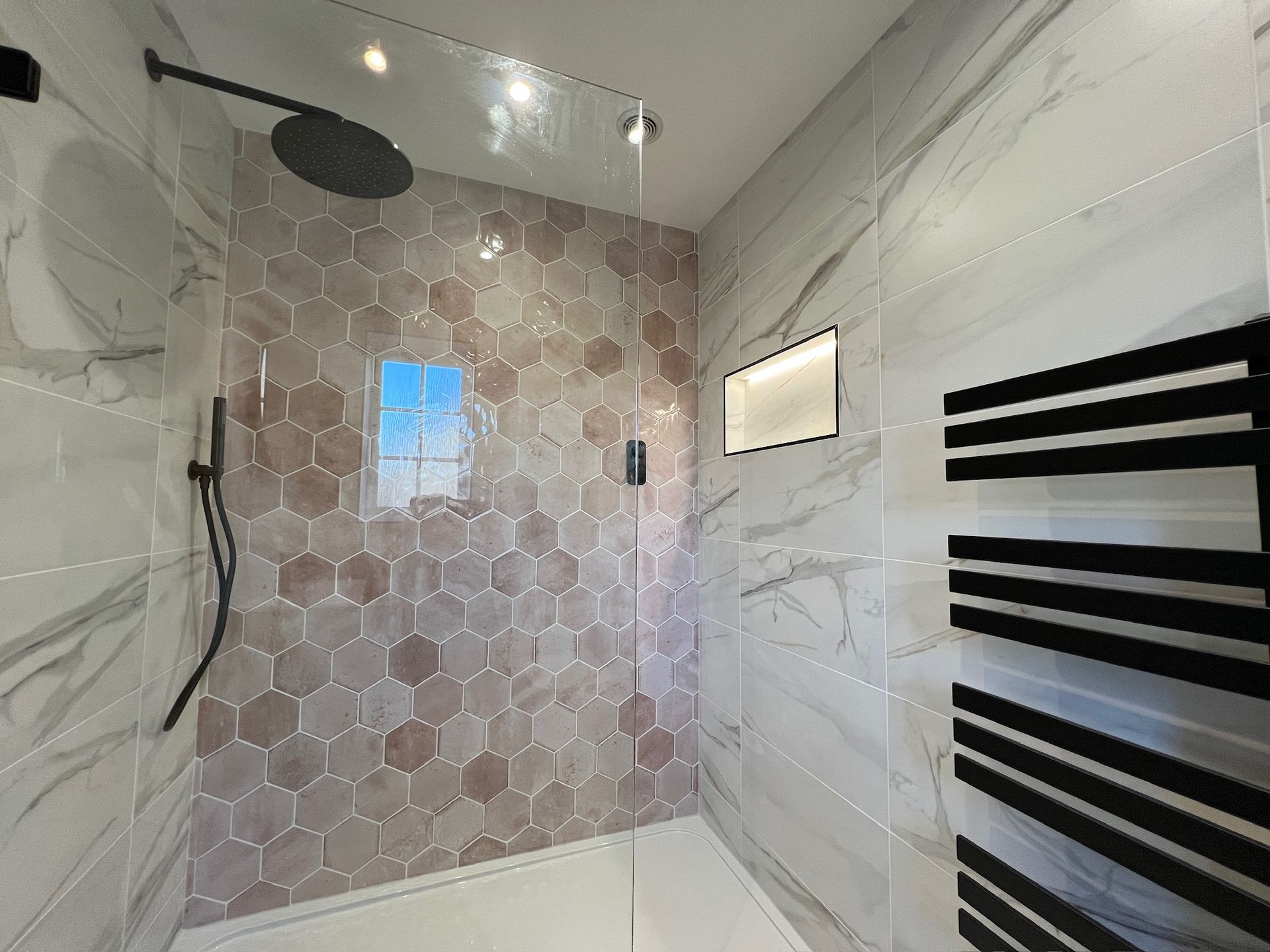 A bathroom with a walk in shower and a black towel rack.