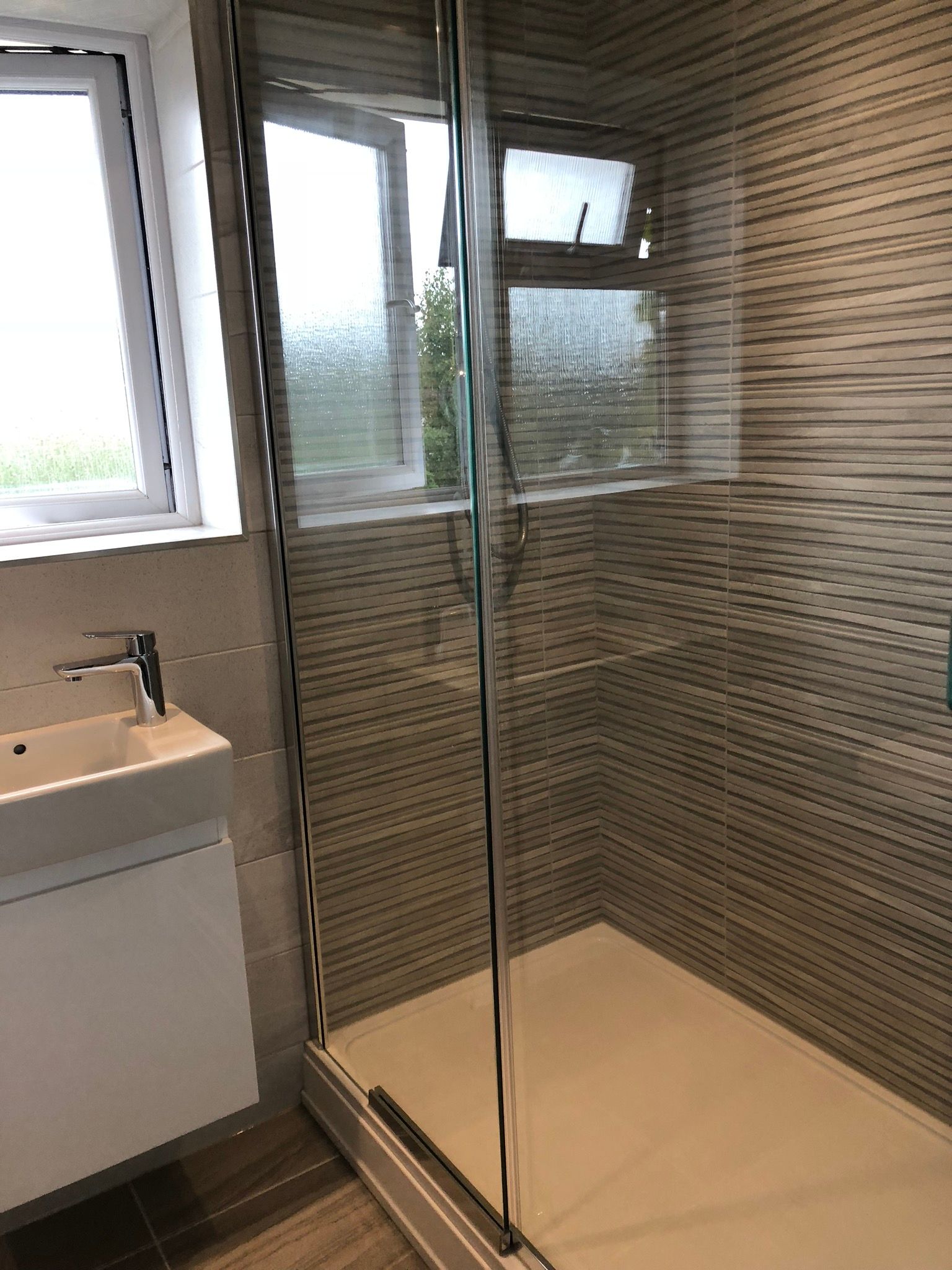 A bathroom with a walk in shower , sink and window.