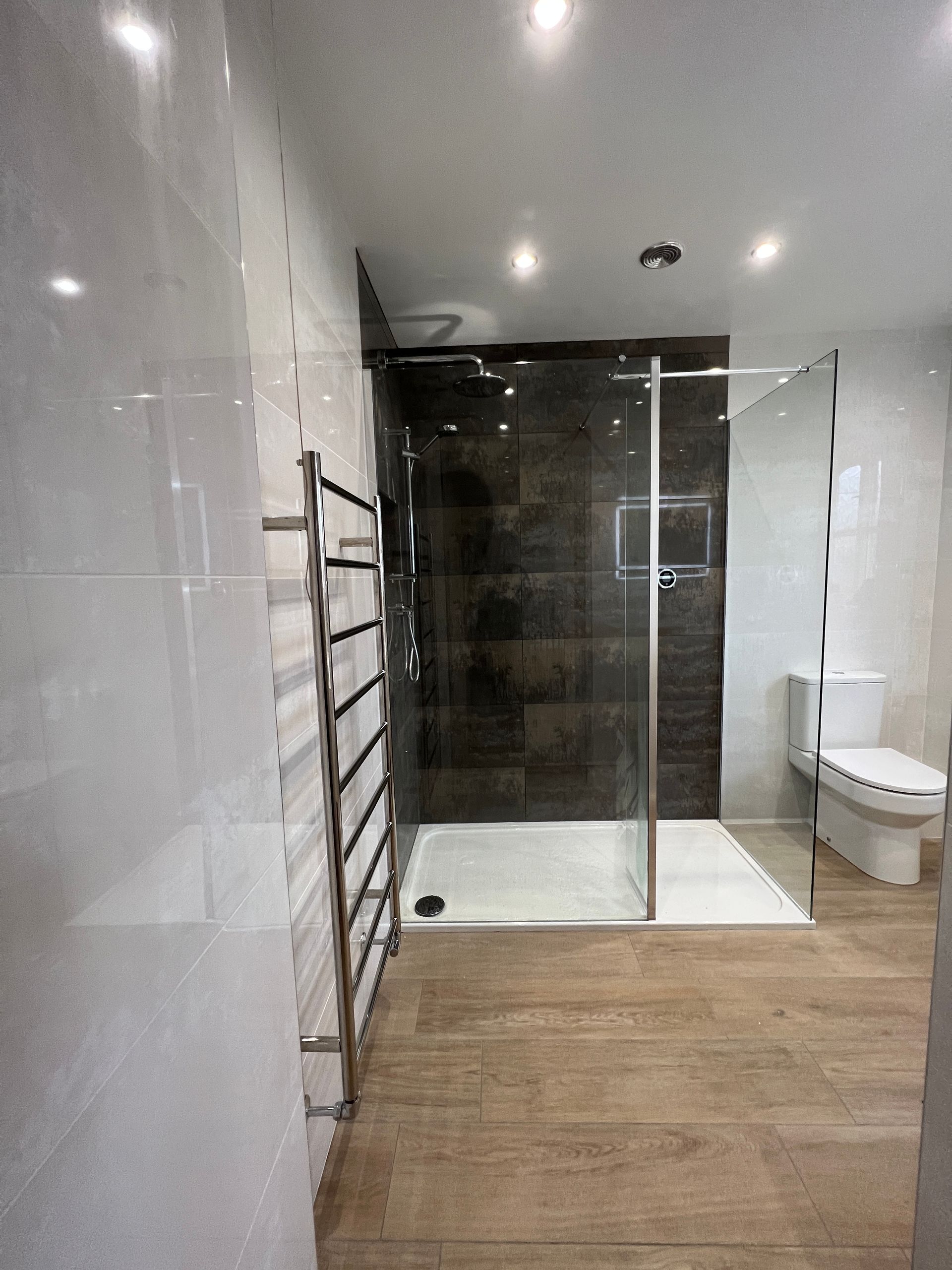 A bathroom with a walk in shower , toilet , and towel rack.