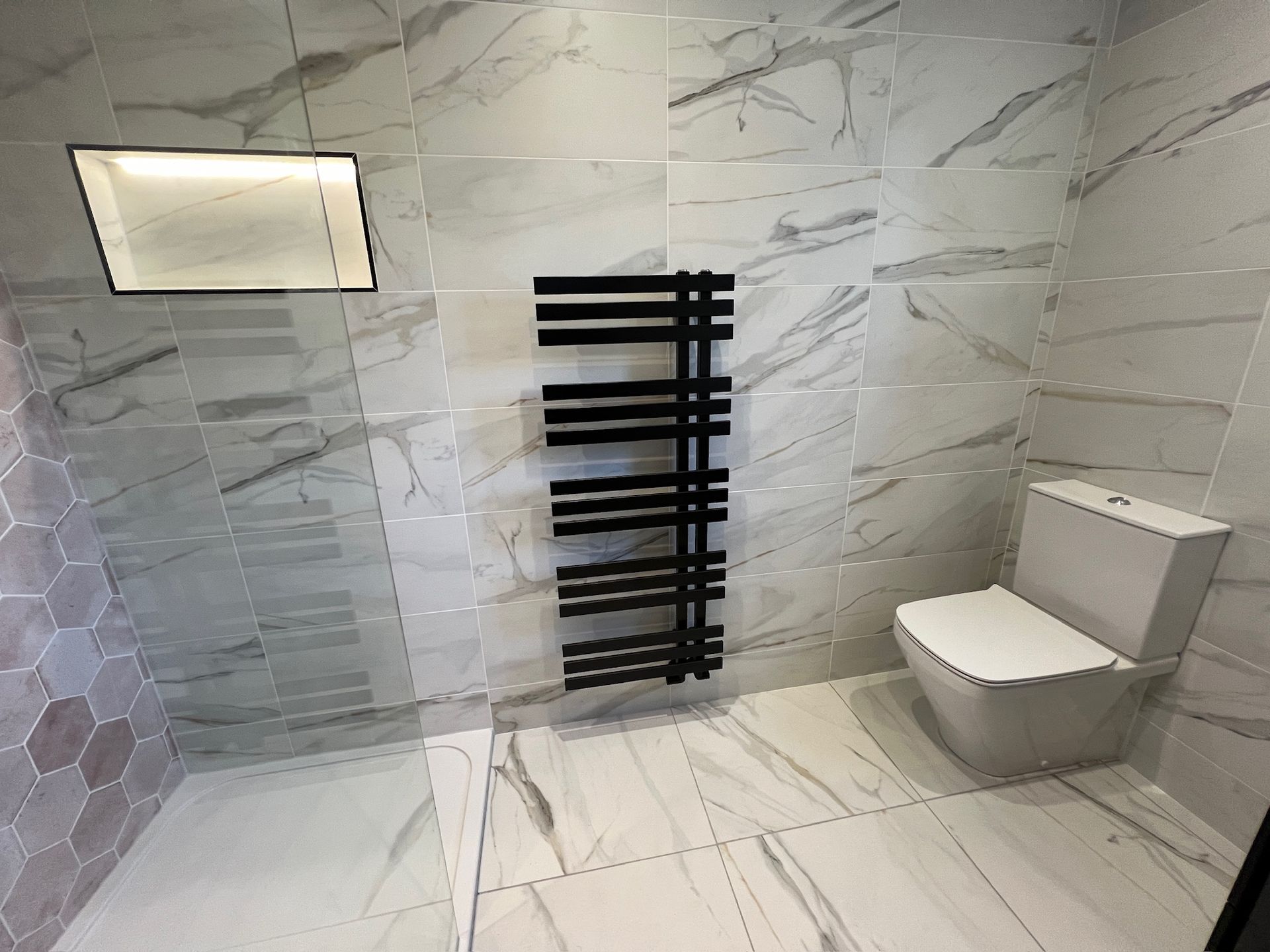 A bathroom with marble tiles , a toilet , and a towel rack.