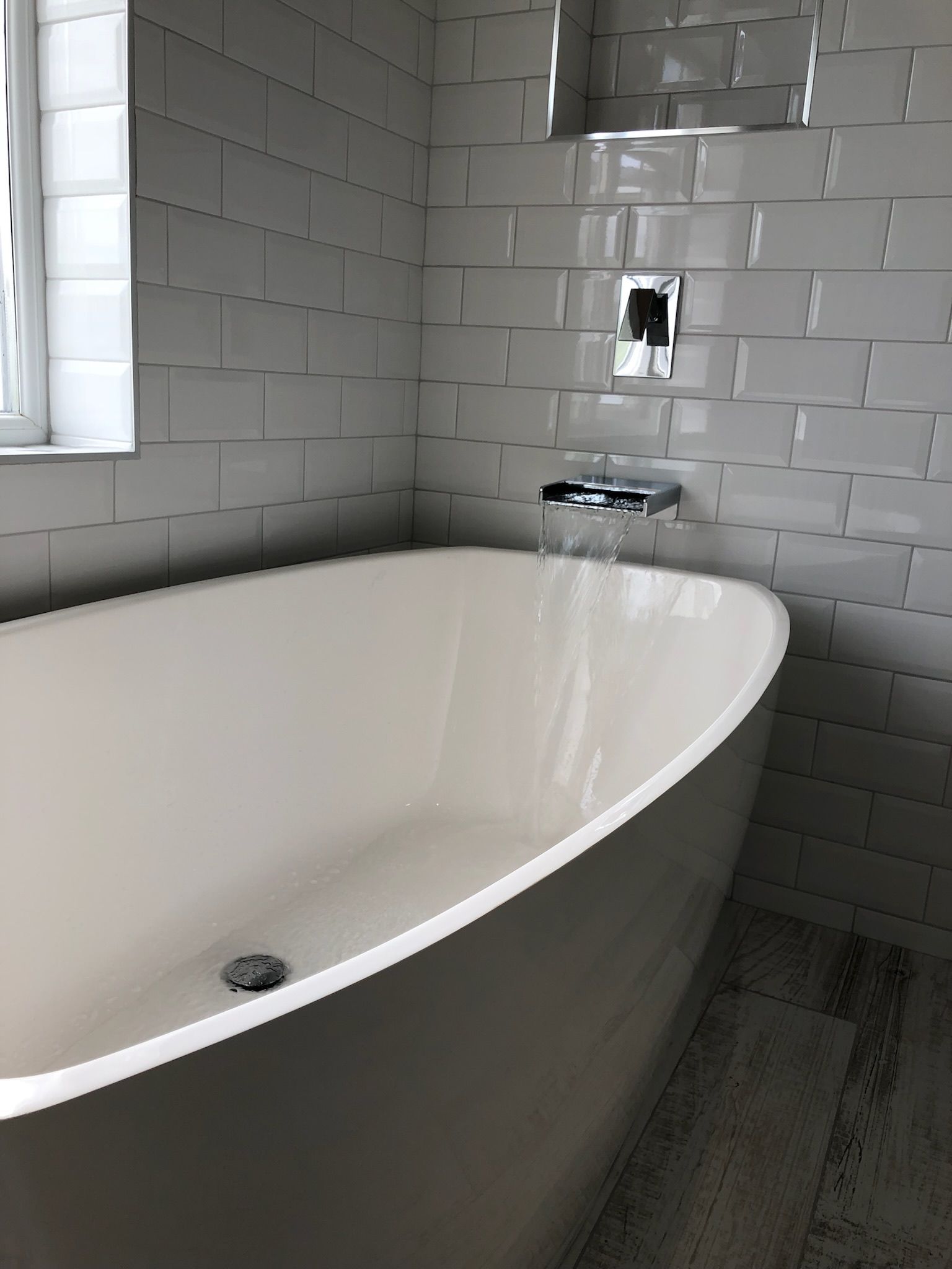 A white bathtub is sitting in a bathroom next to a window.