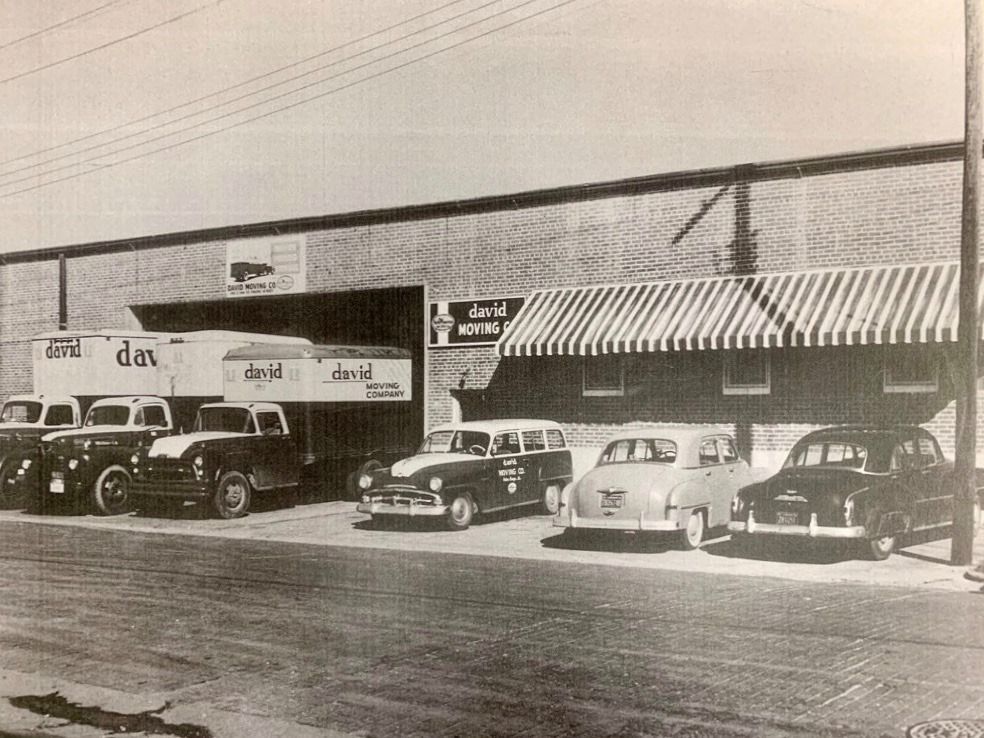 A black and white photo of cars parked in front of a building that says dm