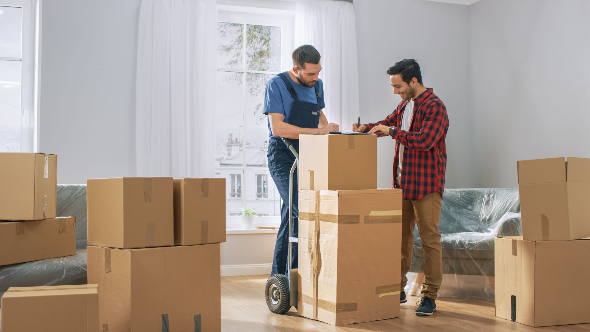 Two men are moving boxes in a living room.