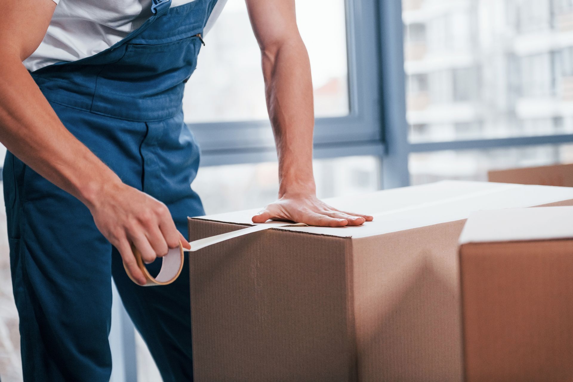 A man is taping a cardboard box with tape.